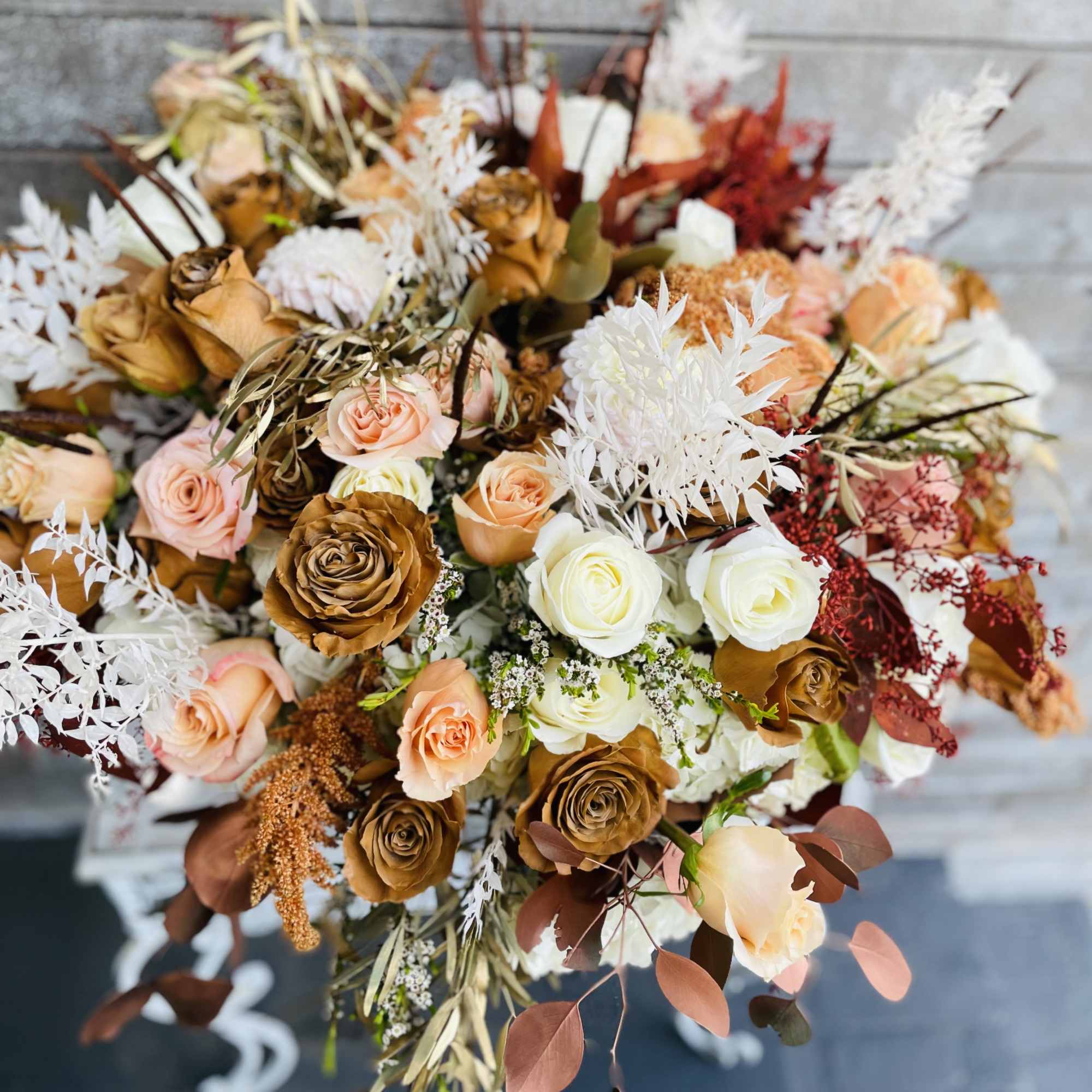 Bouquet of peach, white, and brown roses with dried foliage