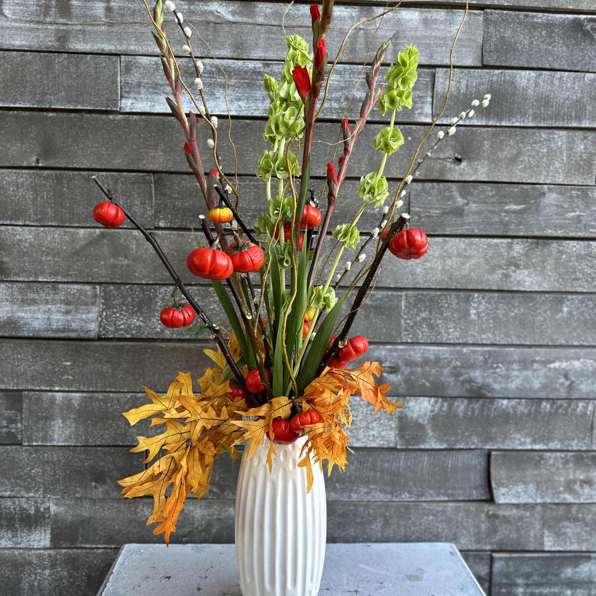 Tall autumn arrangement in a white vase with red accents and orange leaves