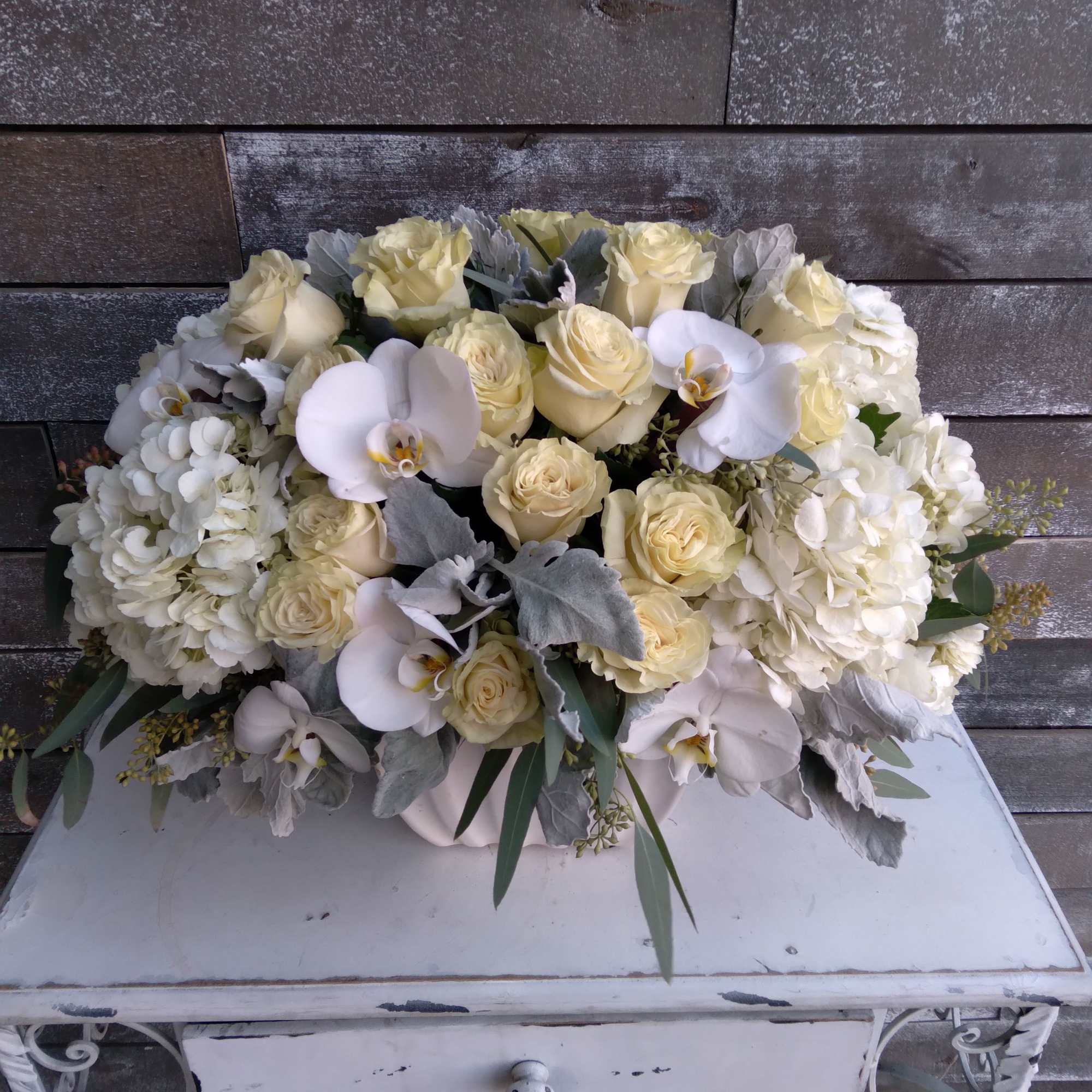 Cream roses and white orchids arranged in a low white container