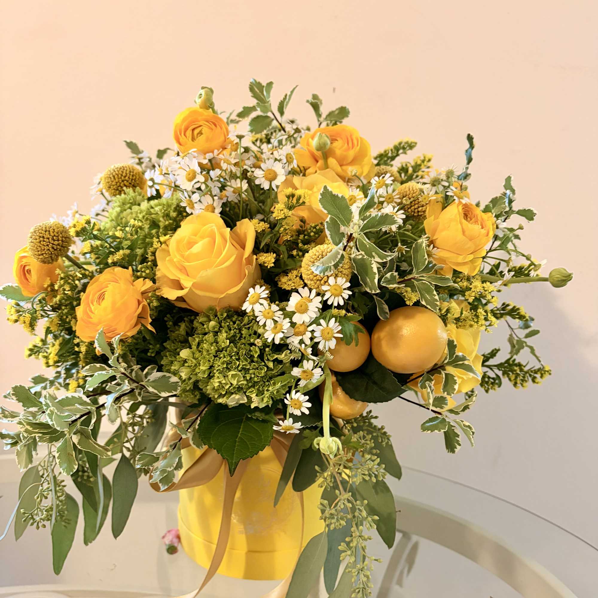Yellow roses and small white daisies in a yellow hatbox arrangement