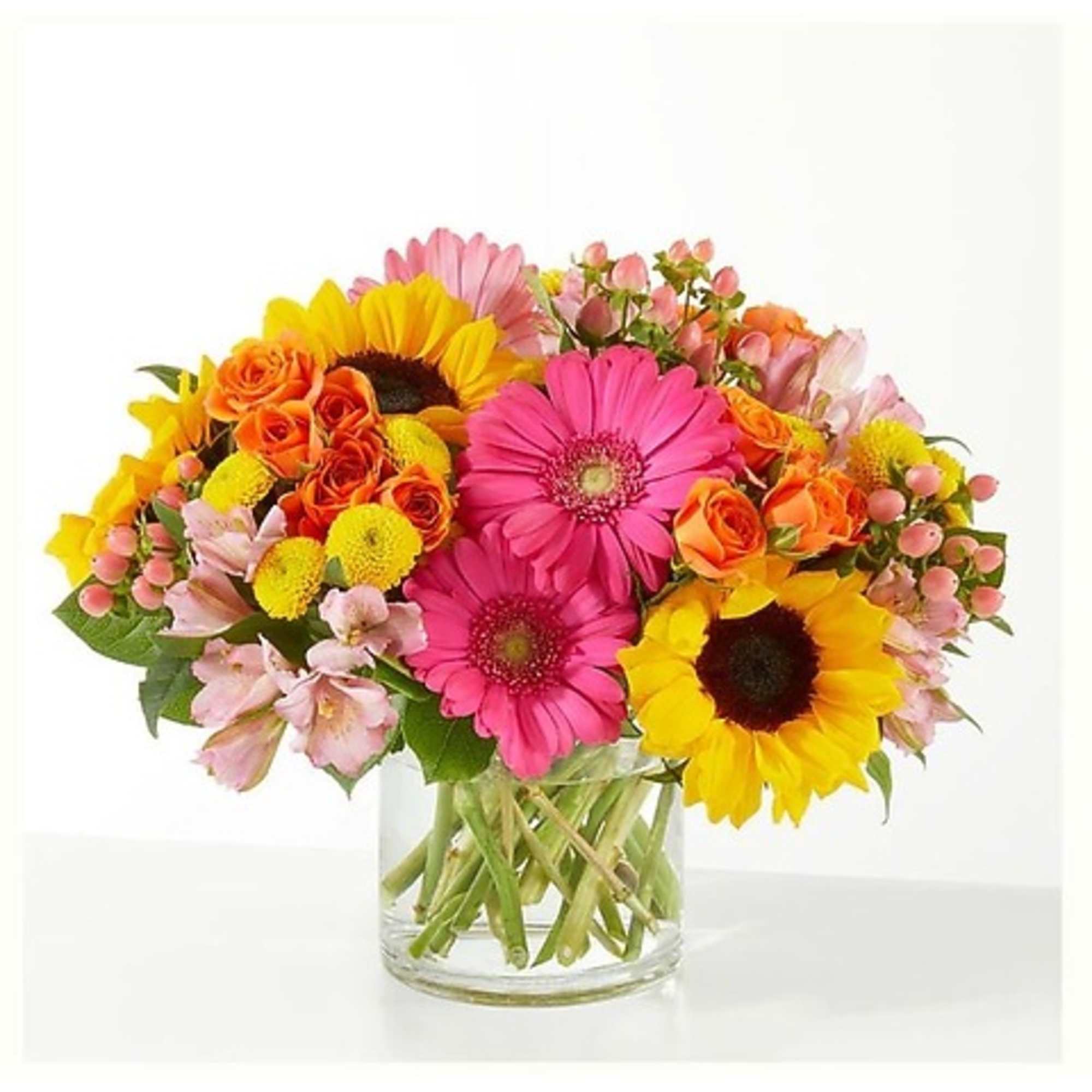 Mixed bouquet of pink gerbera daisies, sunflowers, and orange roses in a glass vase