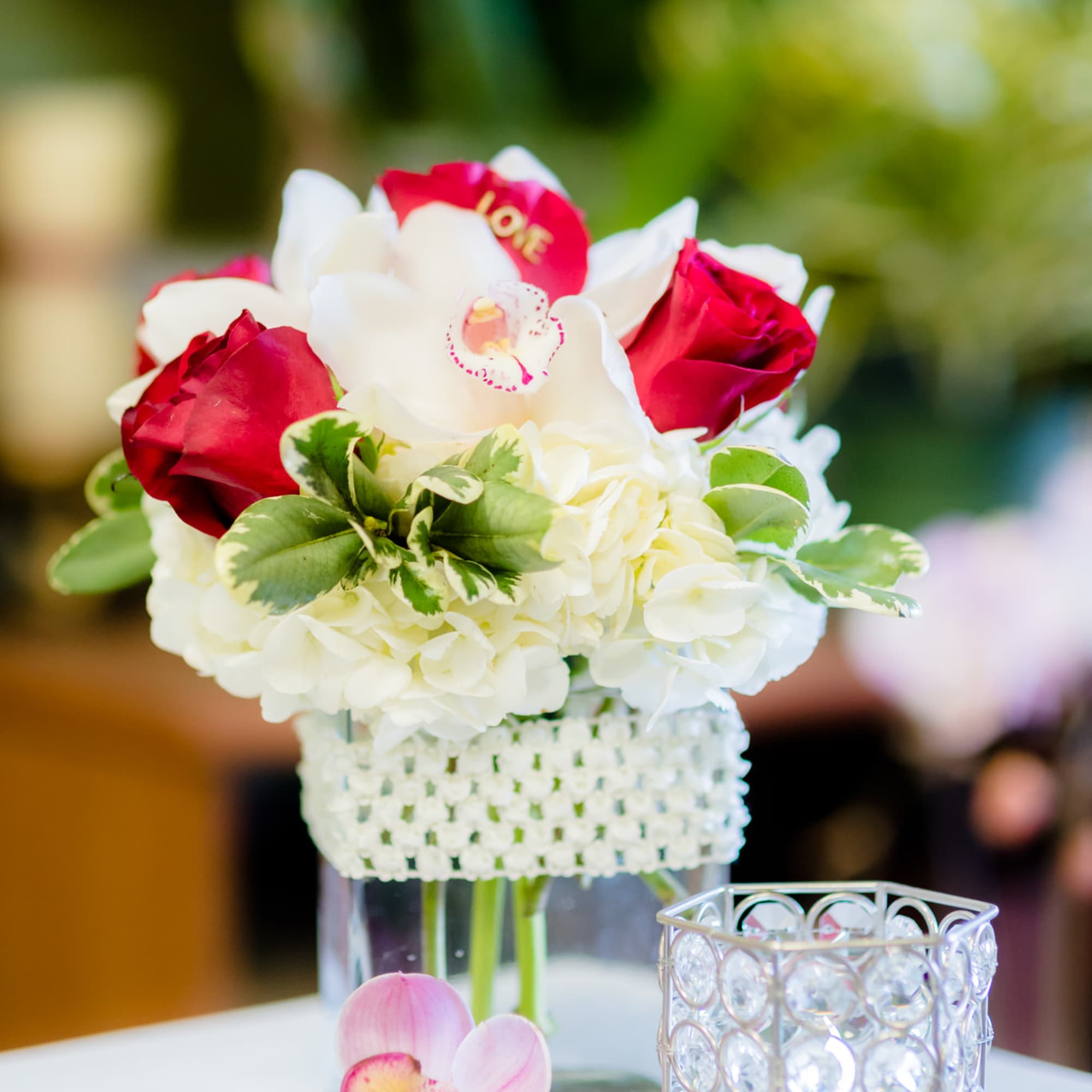 White hydrangea and red roses in a clear vase with a pink orchid bloom