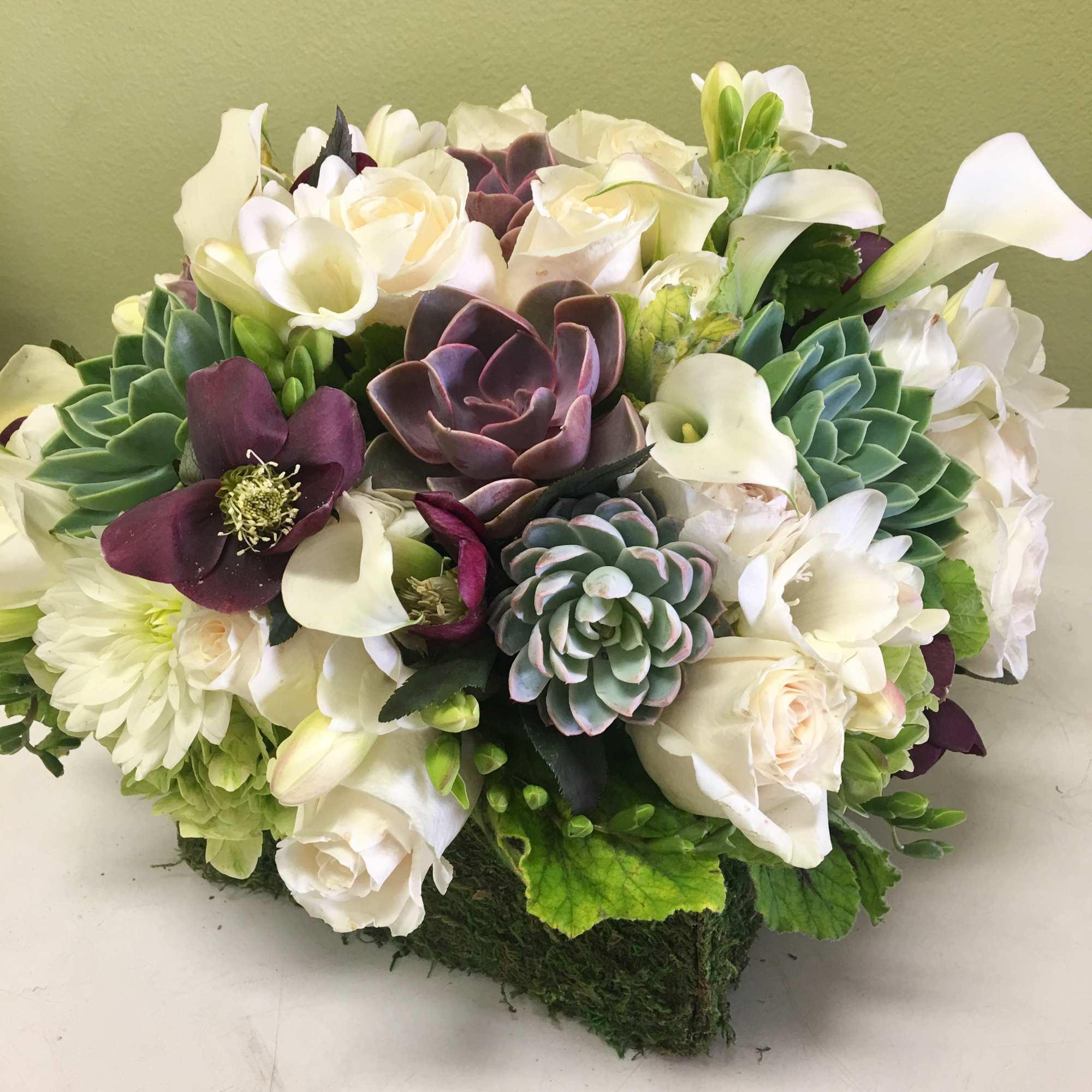 White roses and calla lilies with purple succulents in a low arrangement