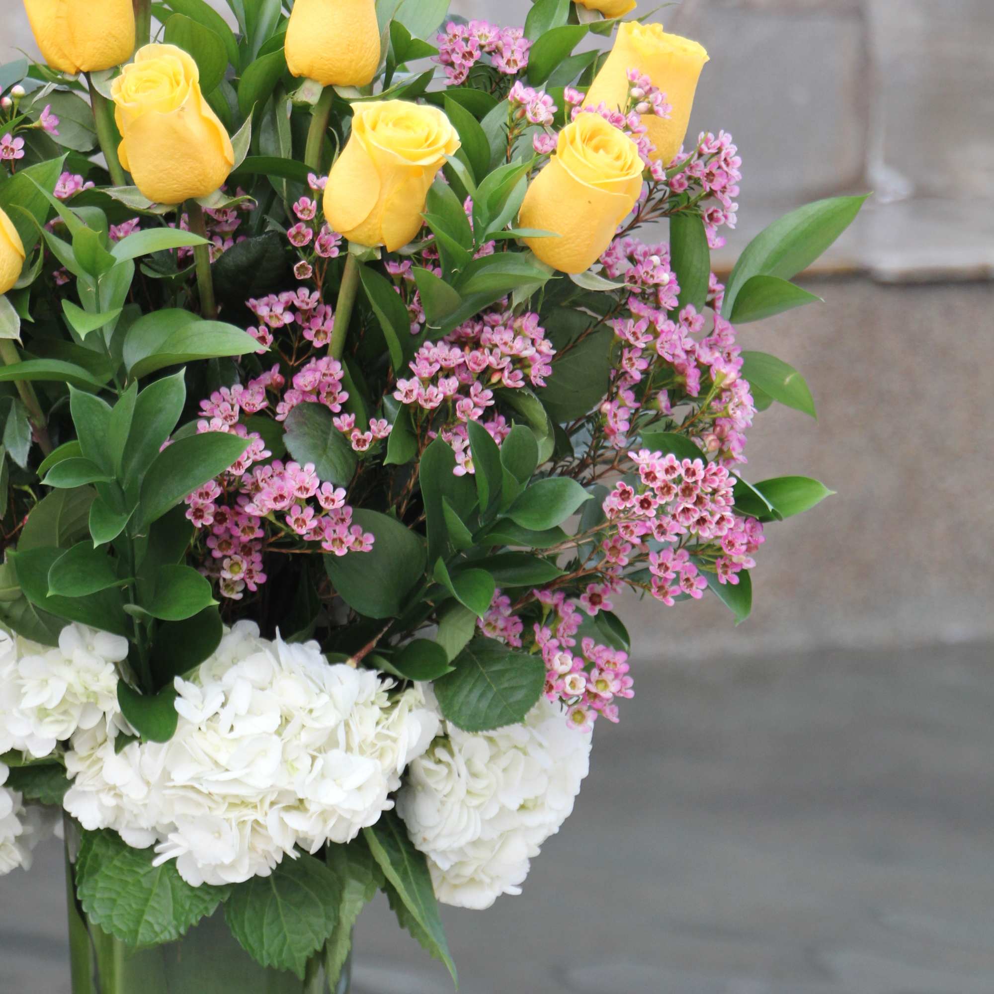 Yellow roses and pink filler flowers arranged in a tall glass vase