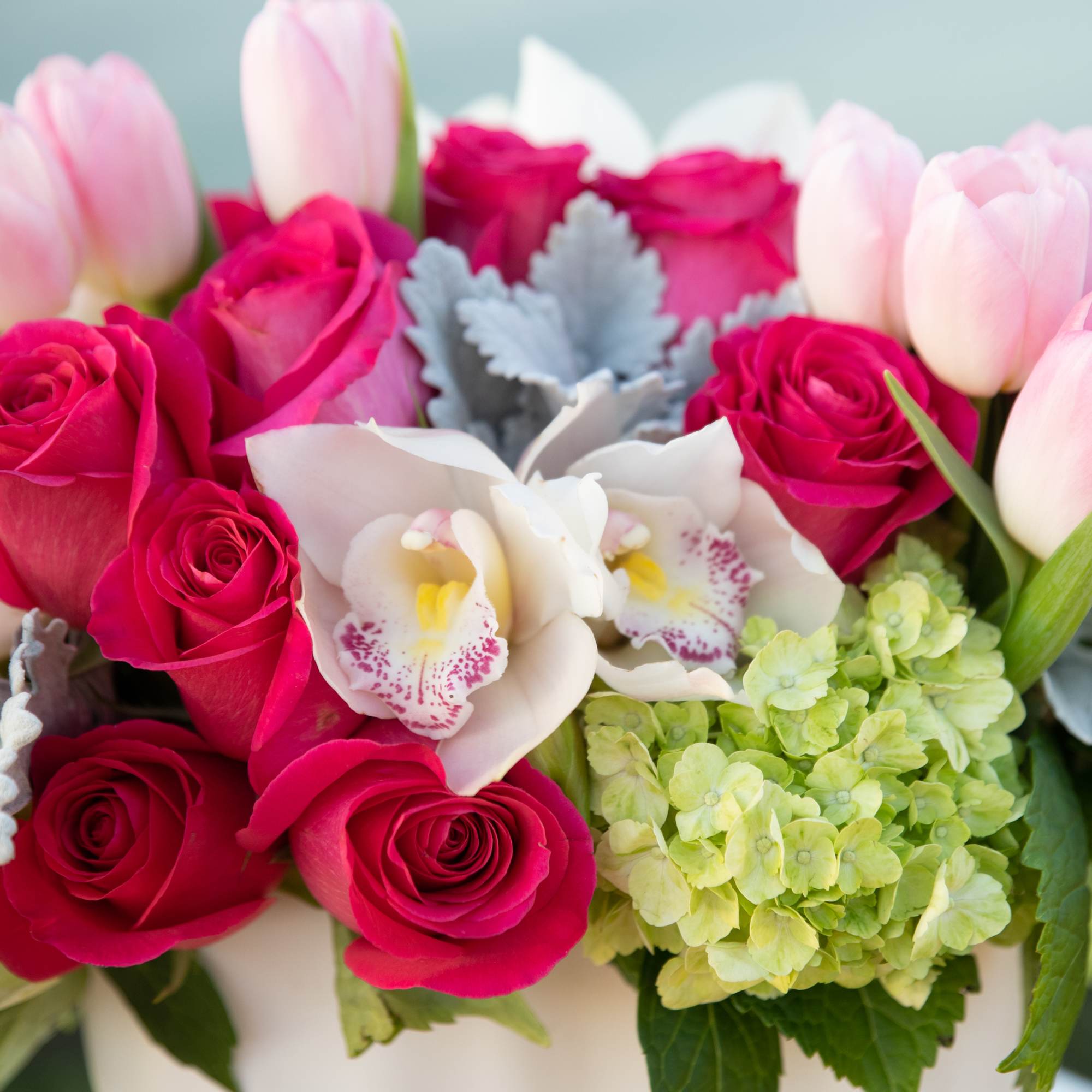 Pink roses and tulips arranged with white orchids in a white vase