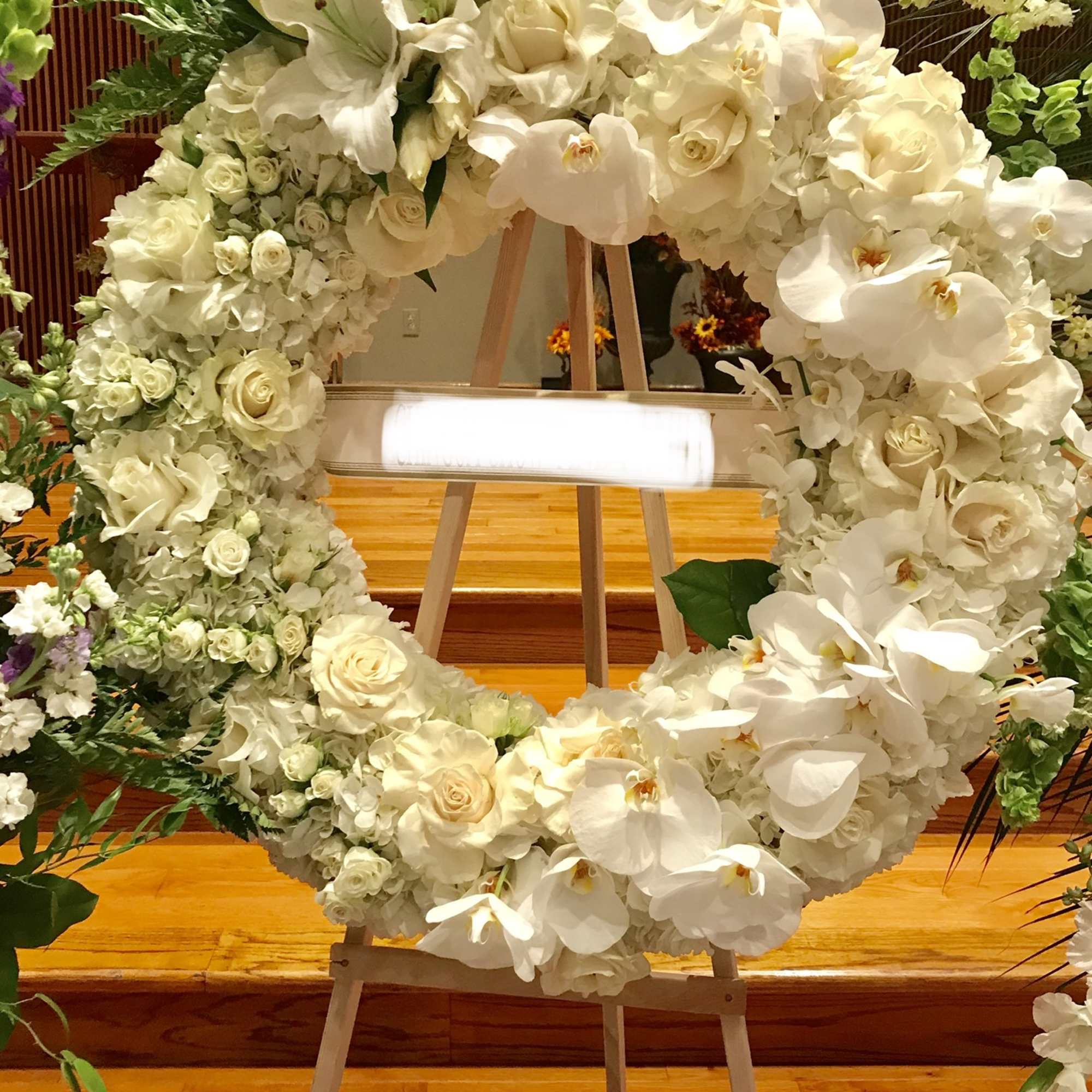 White floral wreath on an easel with roses and orchids