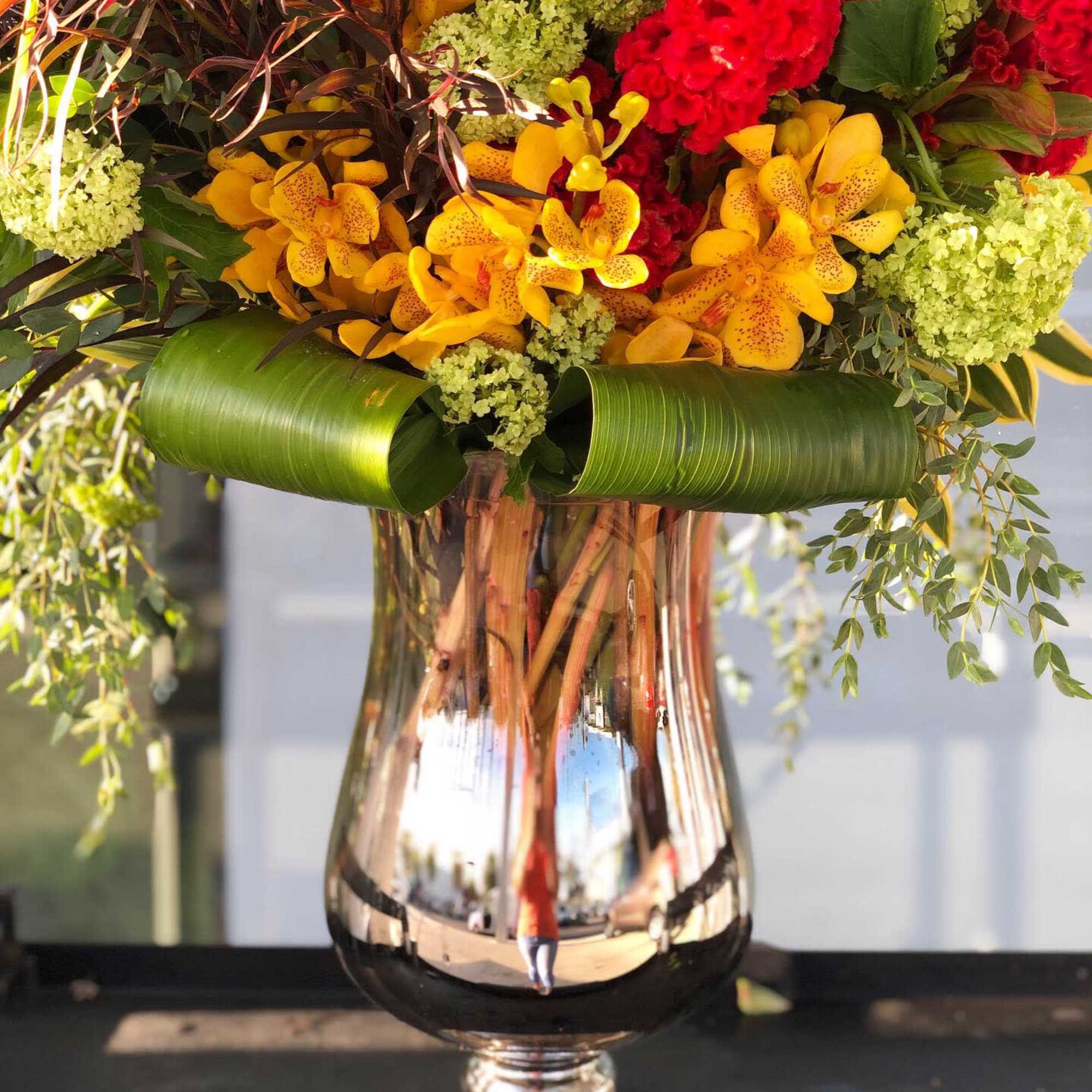Tropical bouquet with yellow orchids and red flowers in a mirrored vase