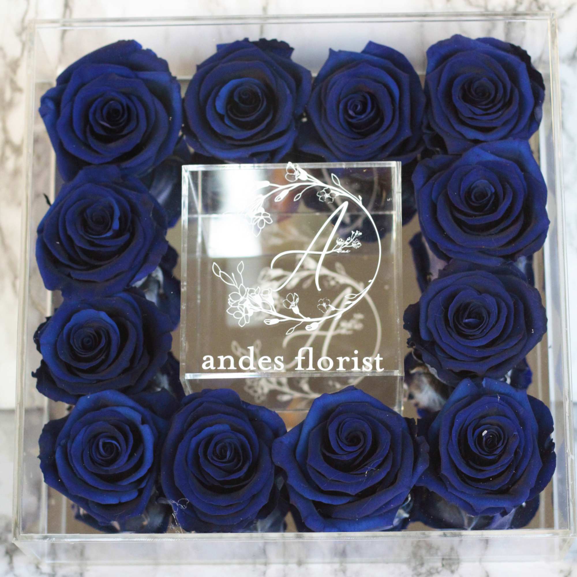 Box of deep blue roses arranged around a clear center plaque