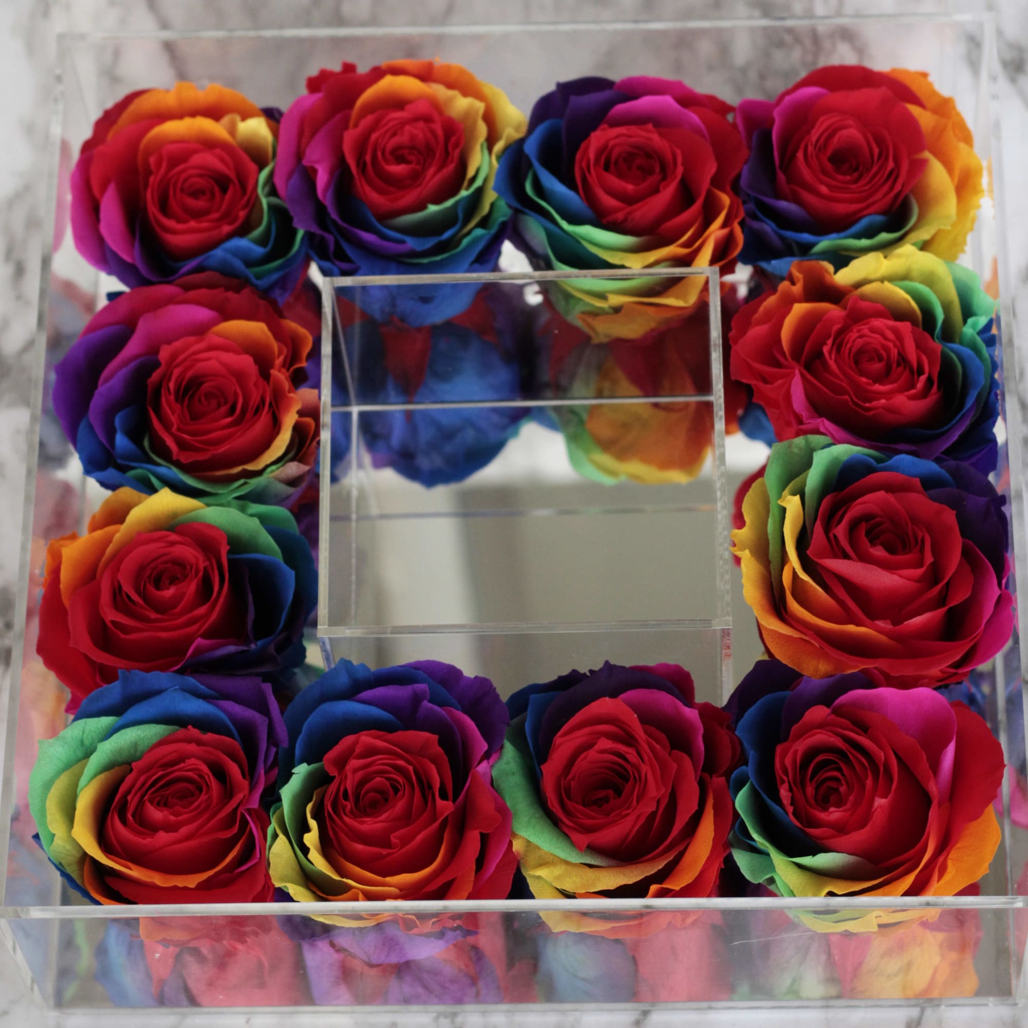 Box of rainbow-colored roses arranged around a clear center compartment