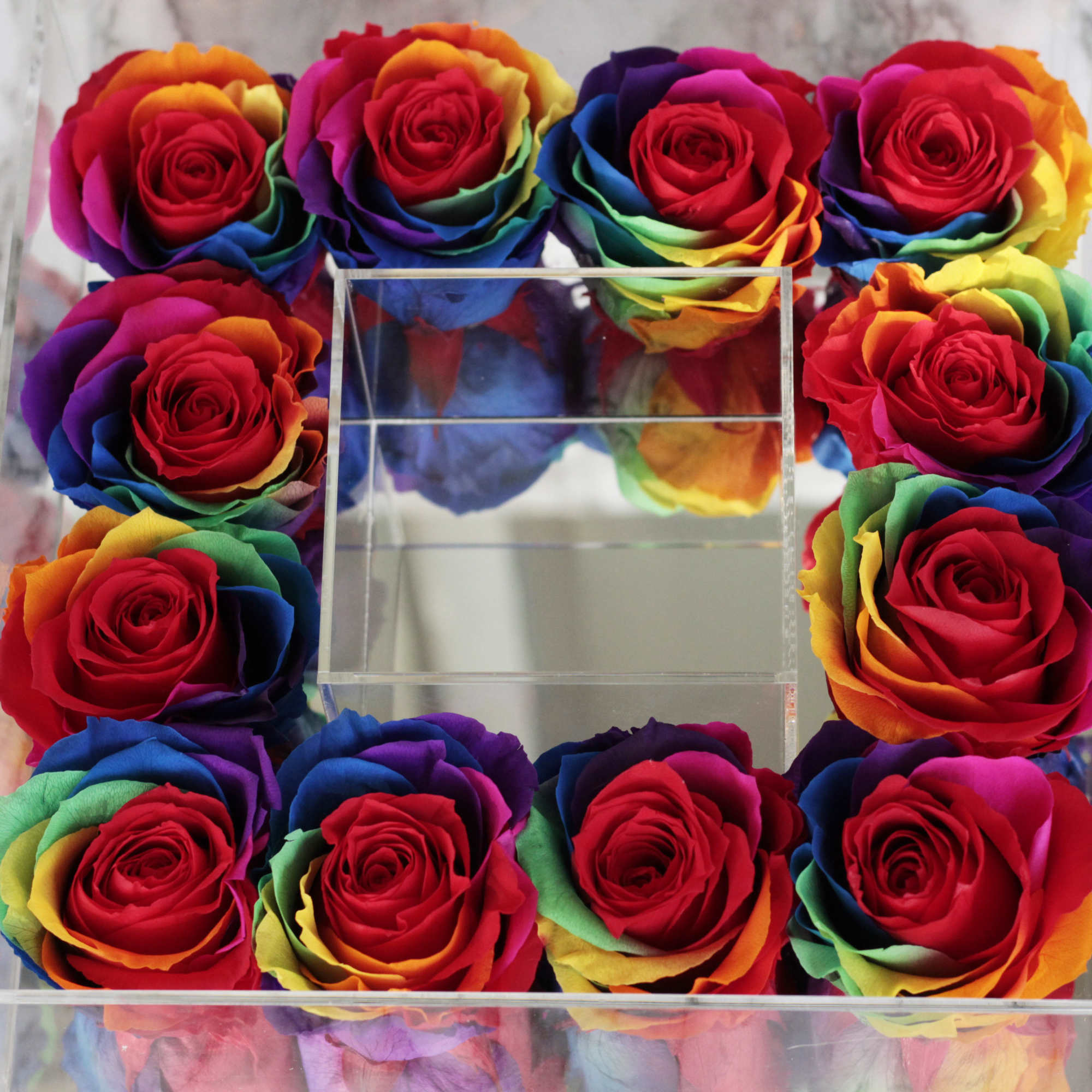 Rainbow-colored roses arranged in a clear square box