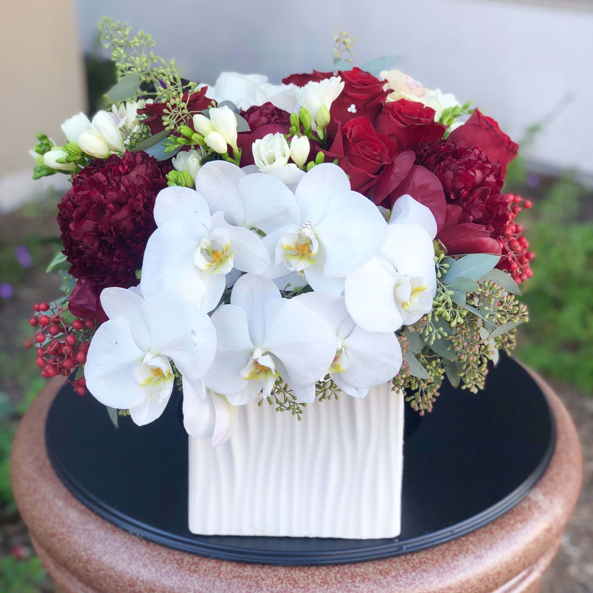 White orchids and red roses in a ribbed white vase