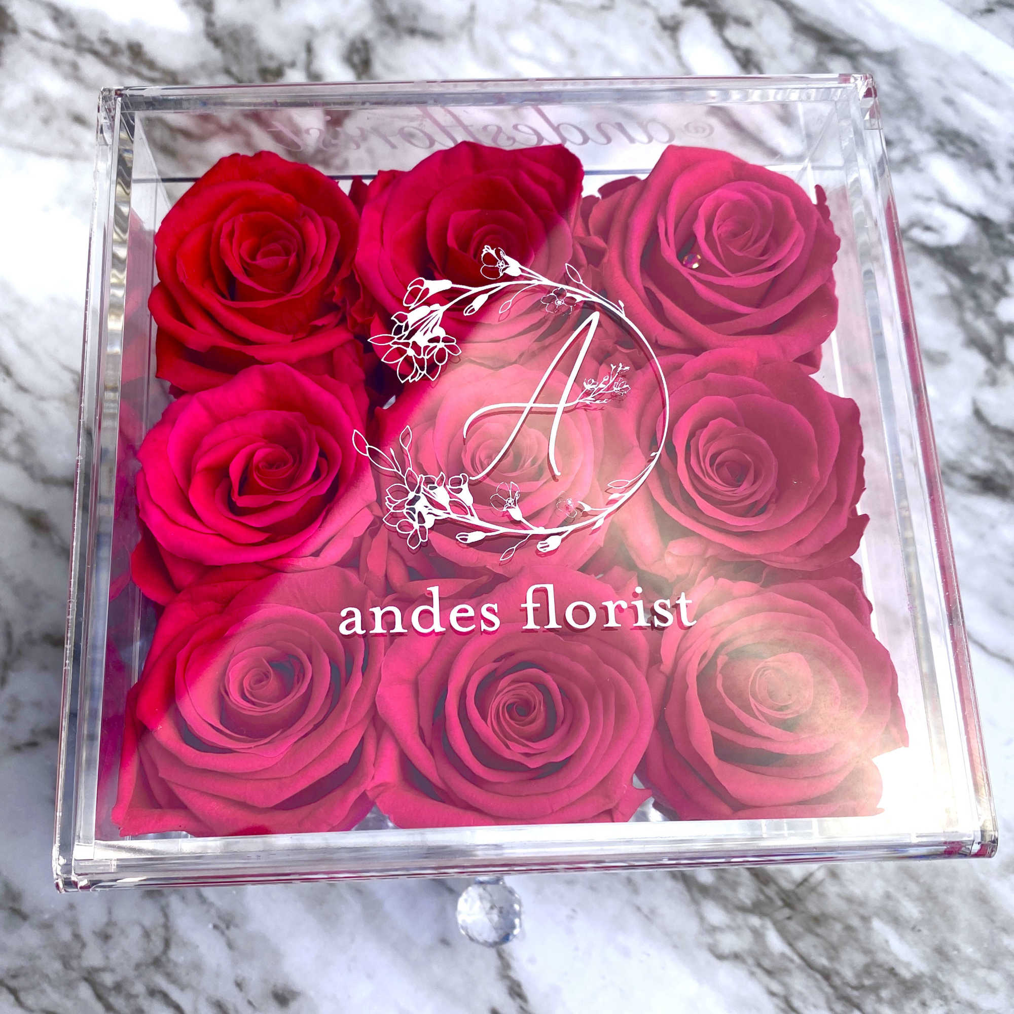 Clear box of pink and red roses with a branded lid