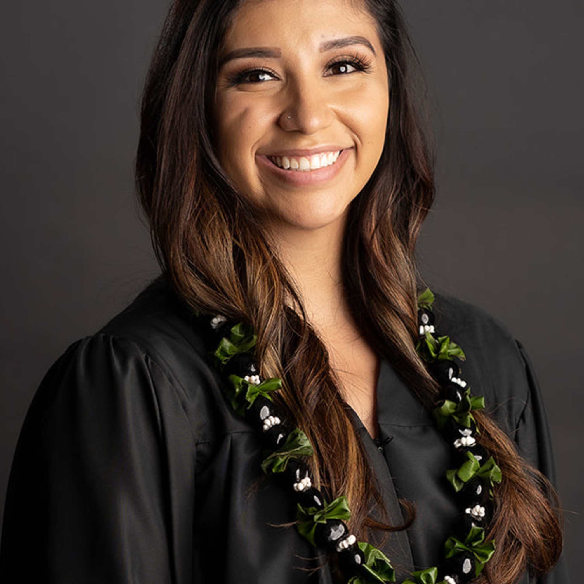 Woman in a black graduation gown wearing a floral lei