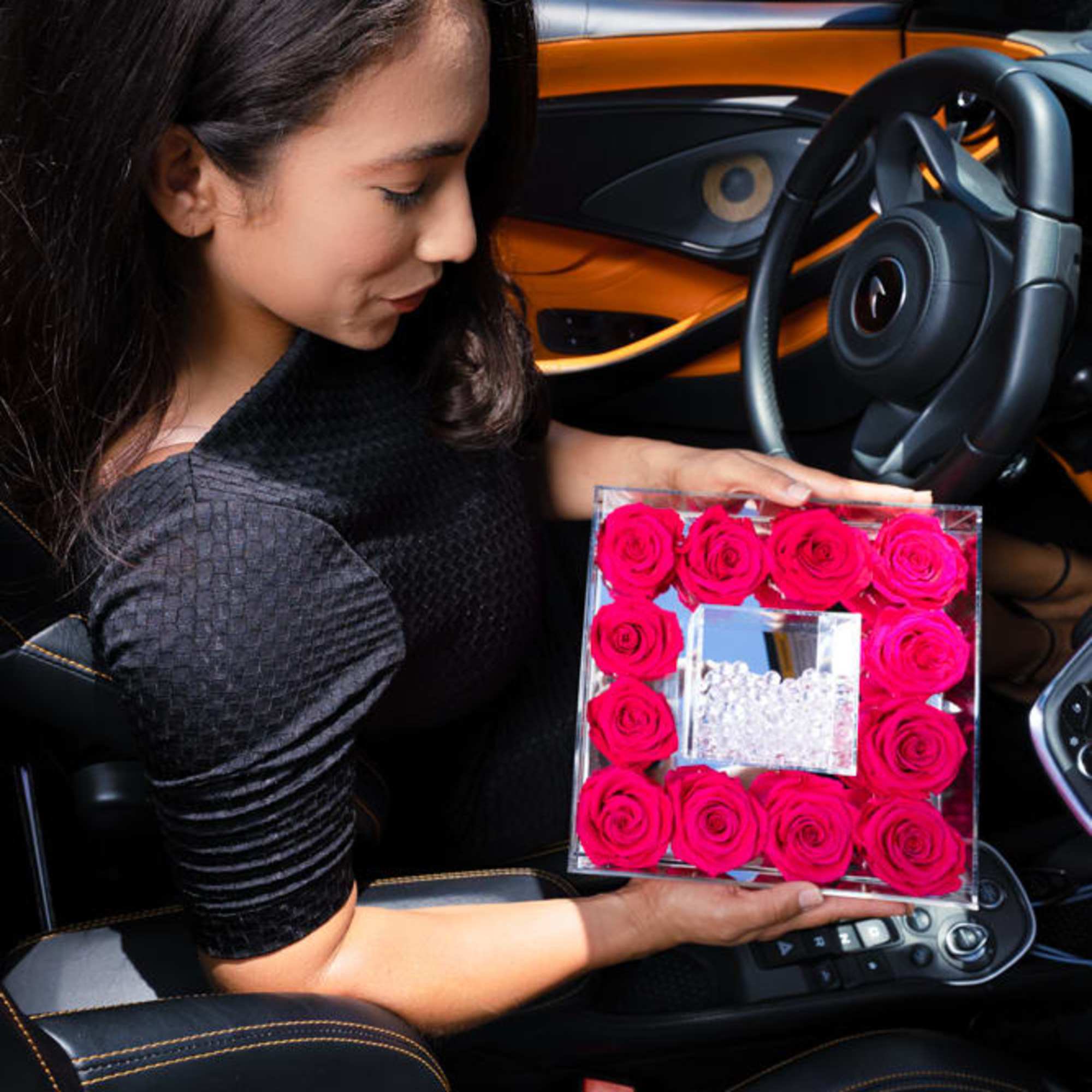 Woman holding a square box of bright pink roses in a car