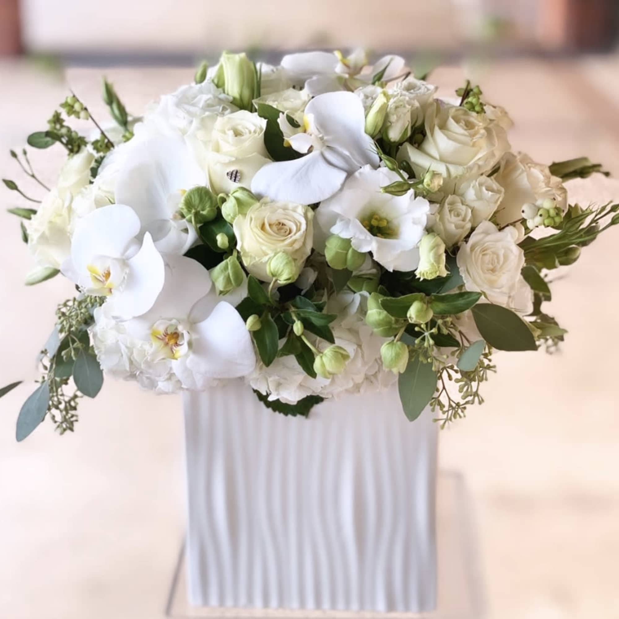 White rose and orchid arrangement in a tall white vase