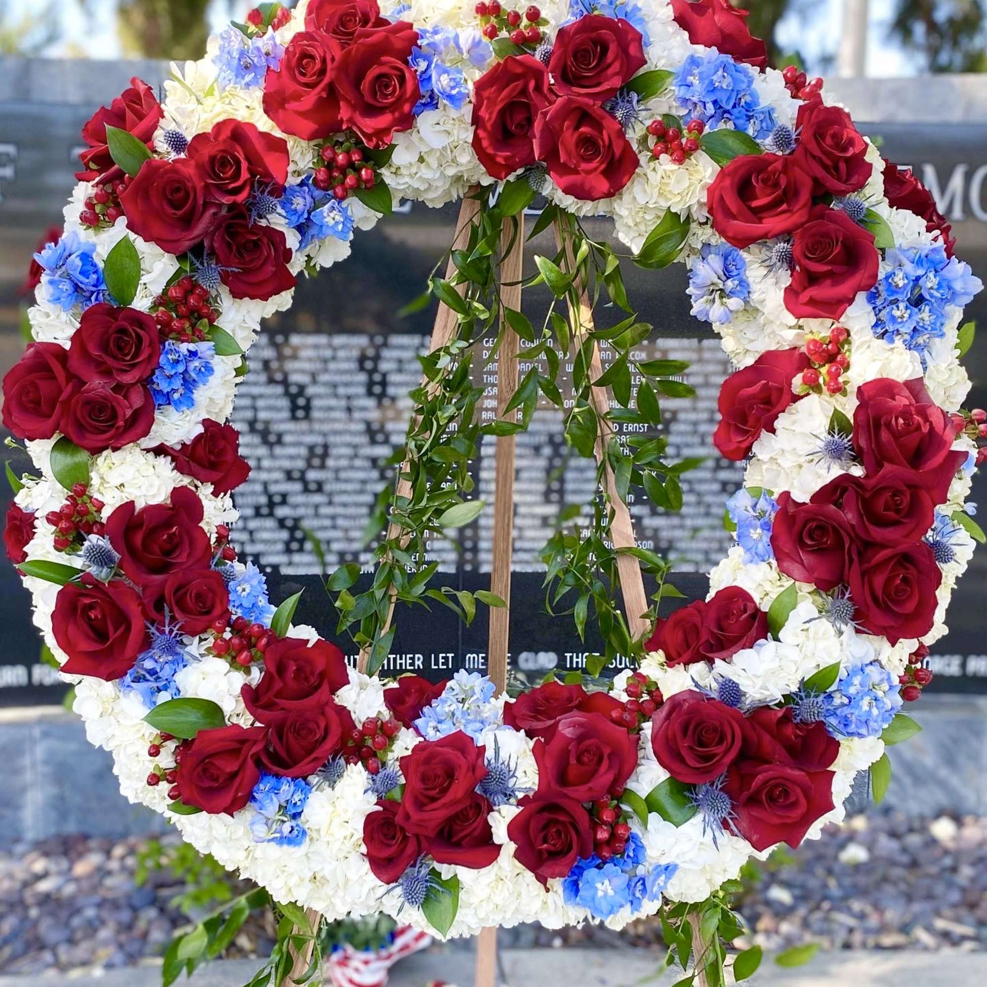 Large floral wreath of red roses, white blooms, and blue flowers on an easel