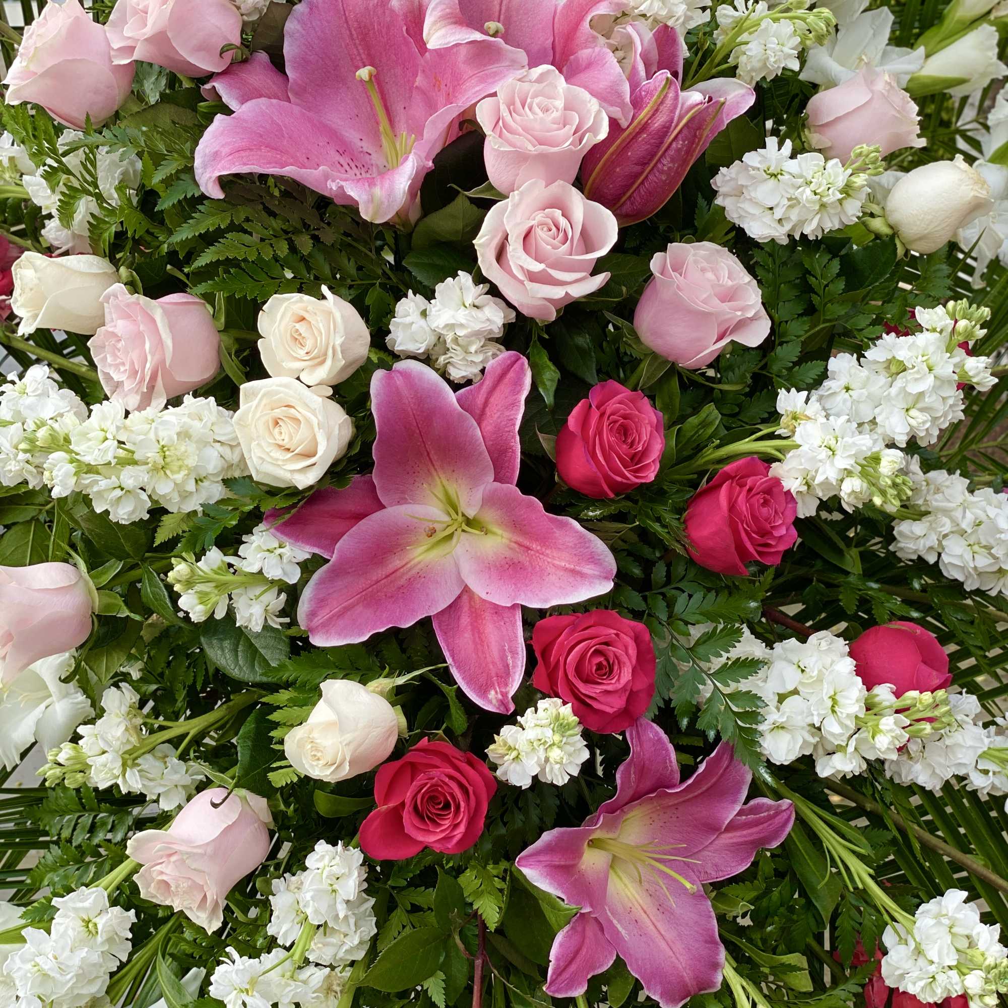 Pink lilies and roses arranged with white blooms and greenery
