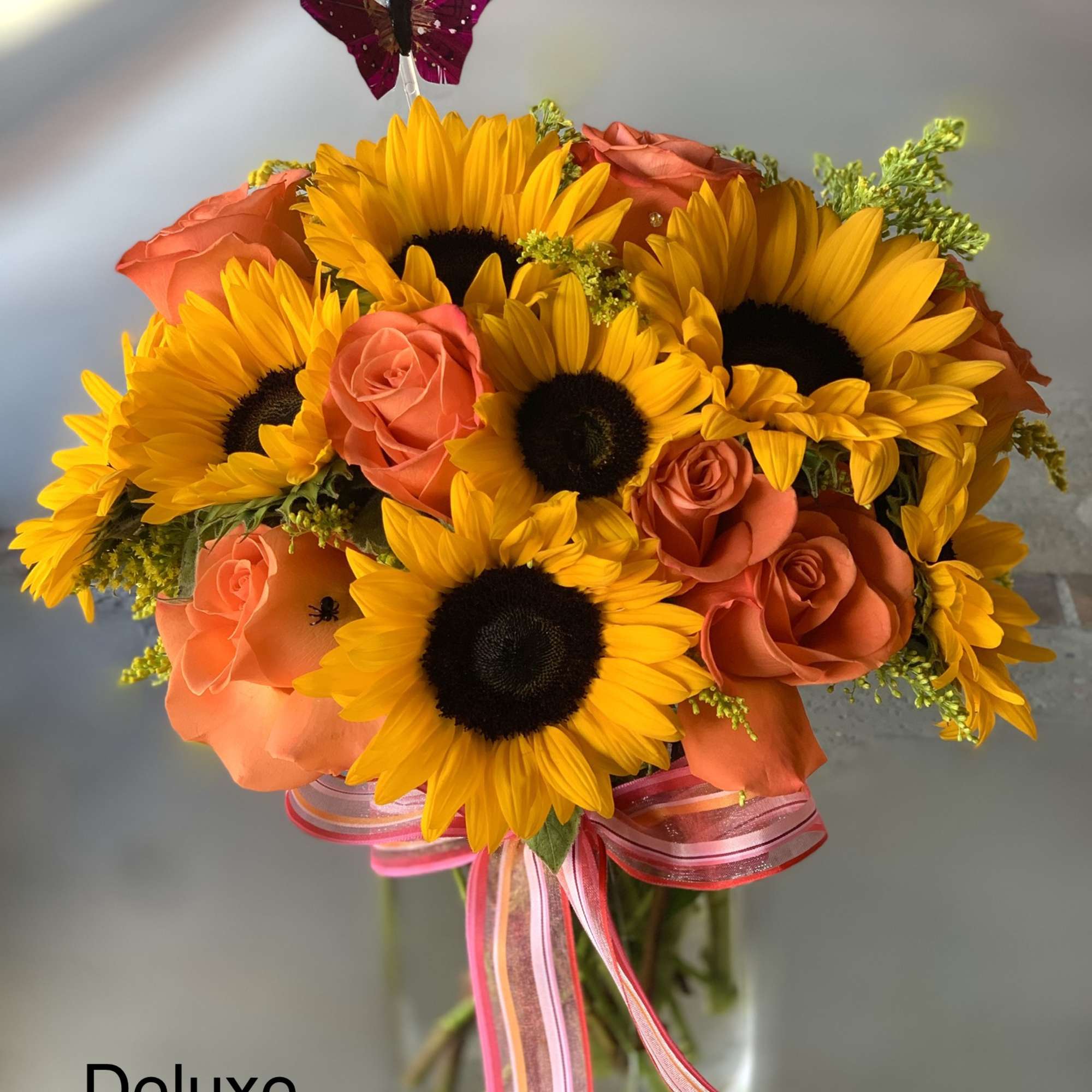 Sunflower and orange rose bouquet in a glass vase with pink ribbon