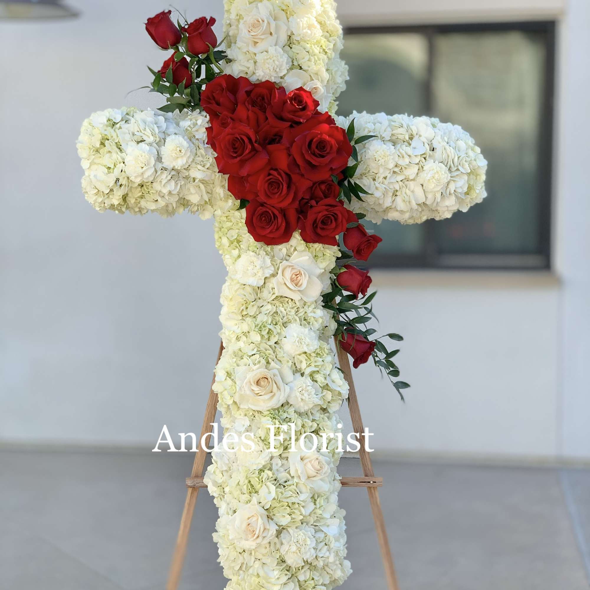 Cross-shaped floral tribute with red and white roses on an easel