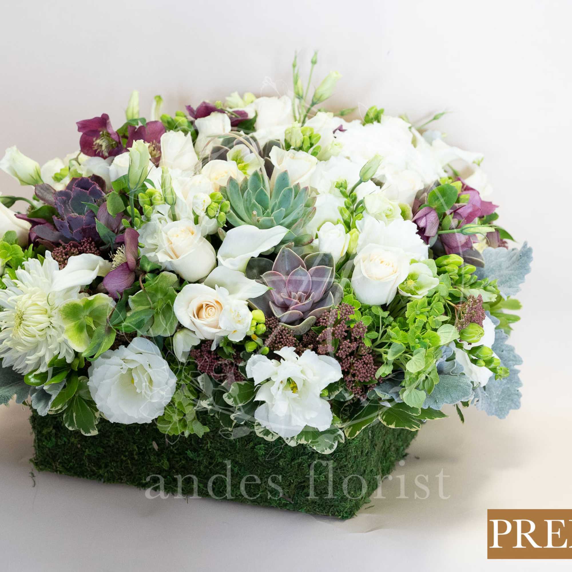 White and purple floral arrangement in a rectangular moss-covered container