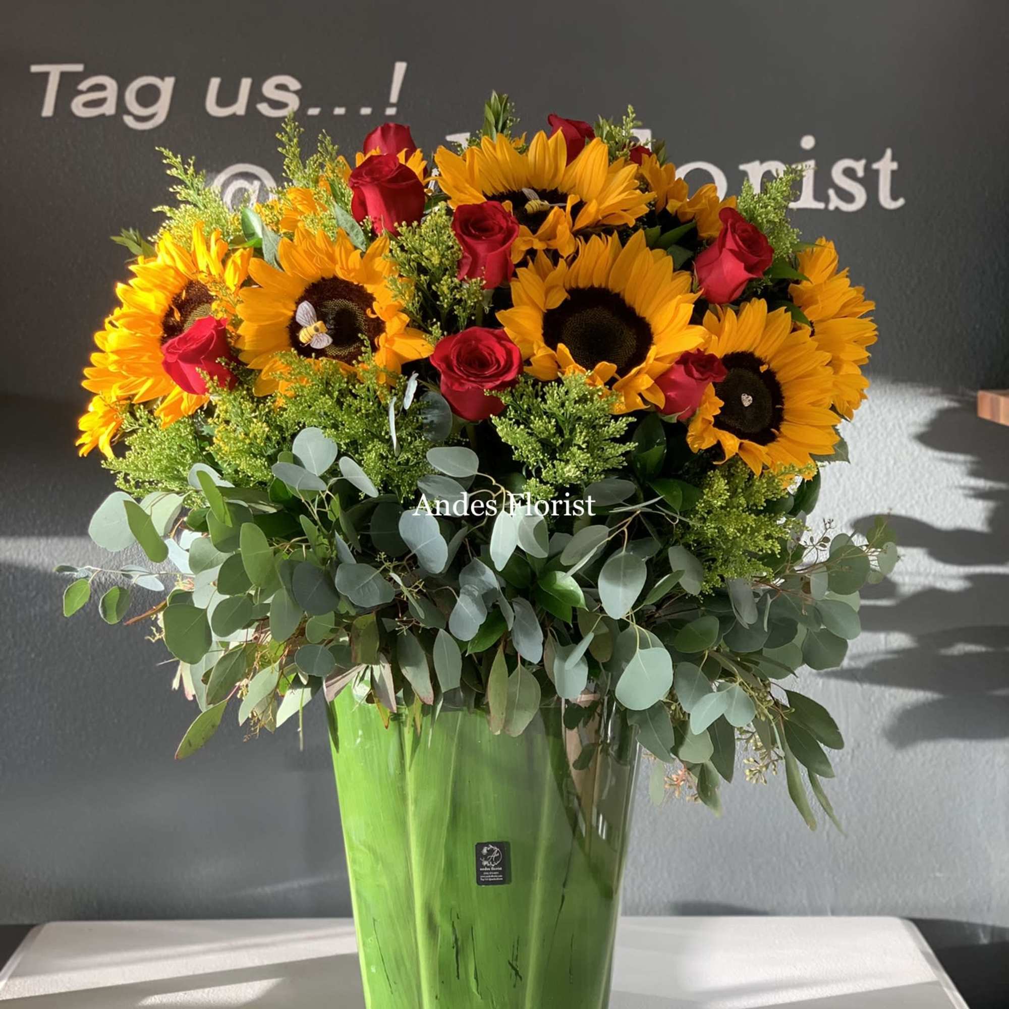 Sunflowers and red roses arranged in a tall green vase