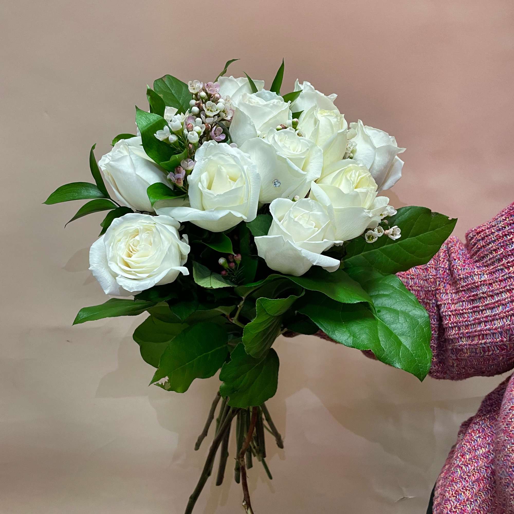 Bouquet of white roses with green foliage and small pink filler flowers