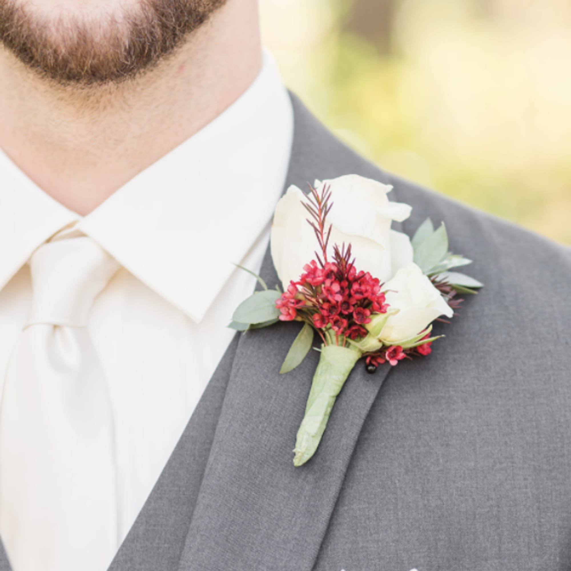 White rose boutonniere with red accents pinned to a gray suit lapel