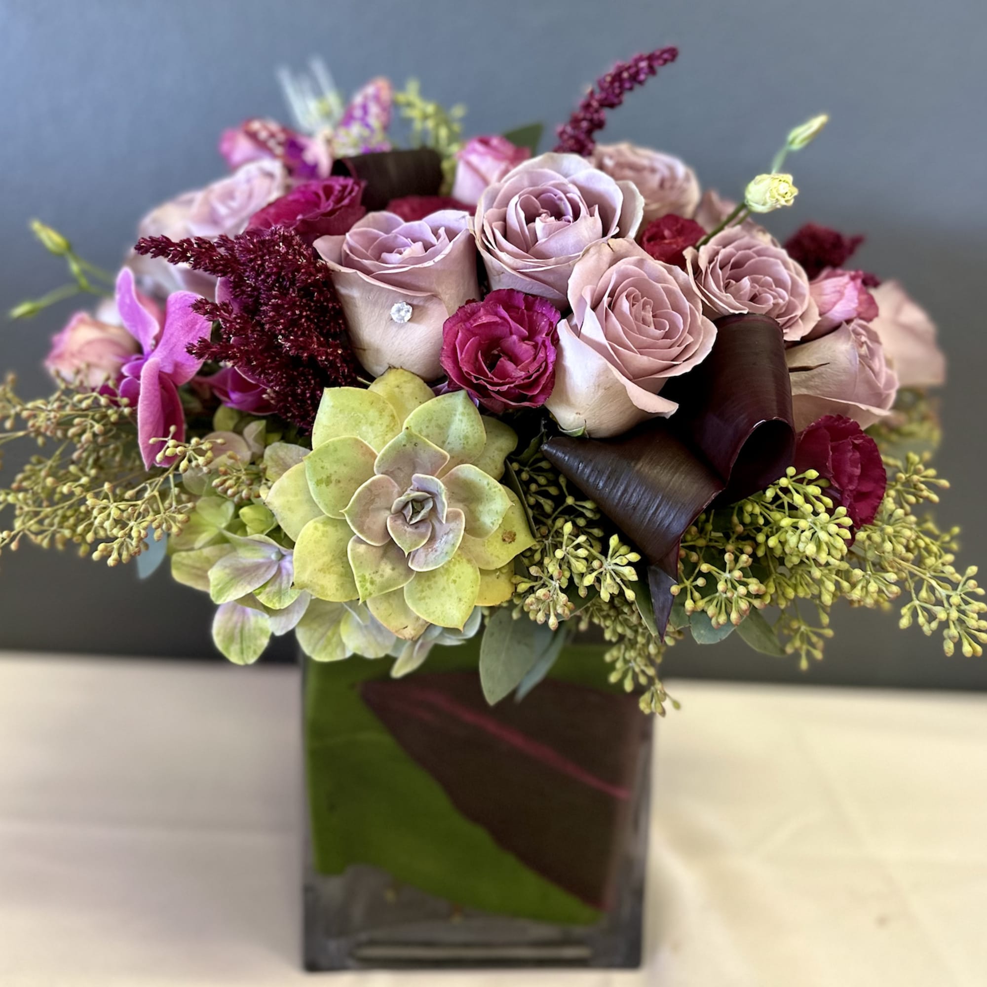 Bouquet of blush roses and succulents in a square glass vase