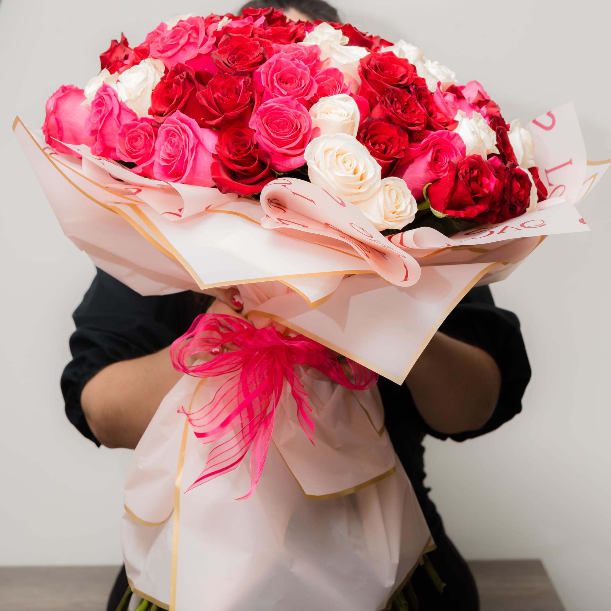 Large bouquet of red, pink, and white roses wrapped in pale paper with a pink ribbon.