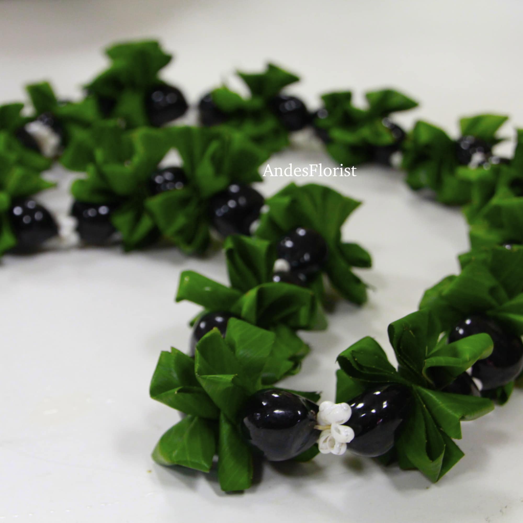 Green leaf lei with black bead accents on a white surface