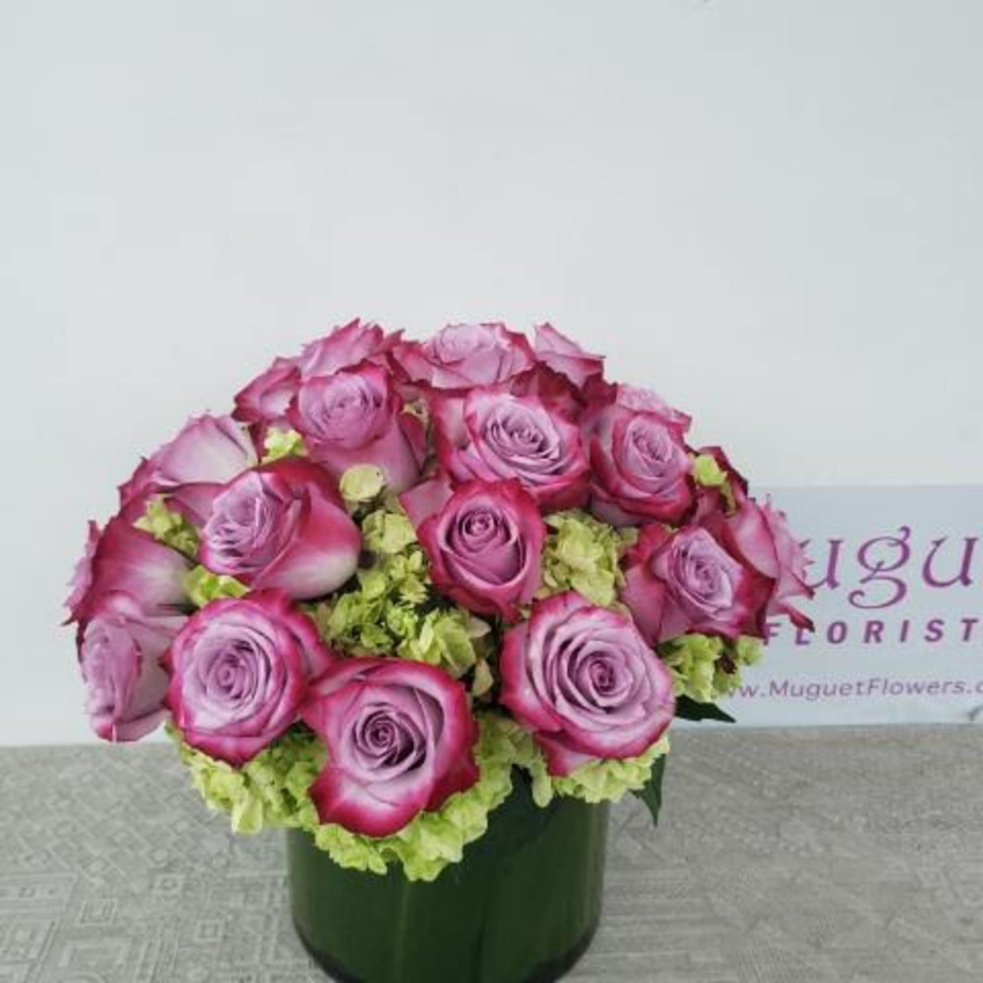 Pink roses arranged in a green vase with light green filler flowers