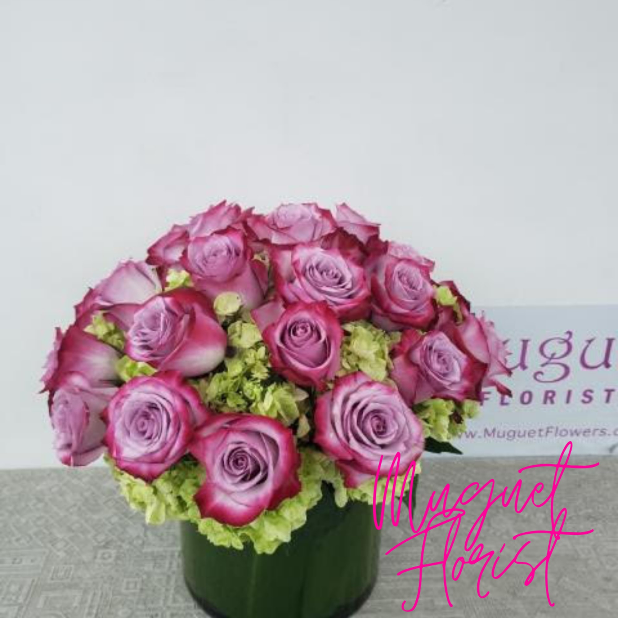 Pink roses arranged in a dark green box with pale green filler flowers.
