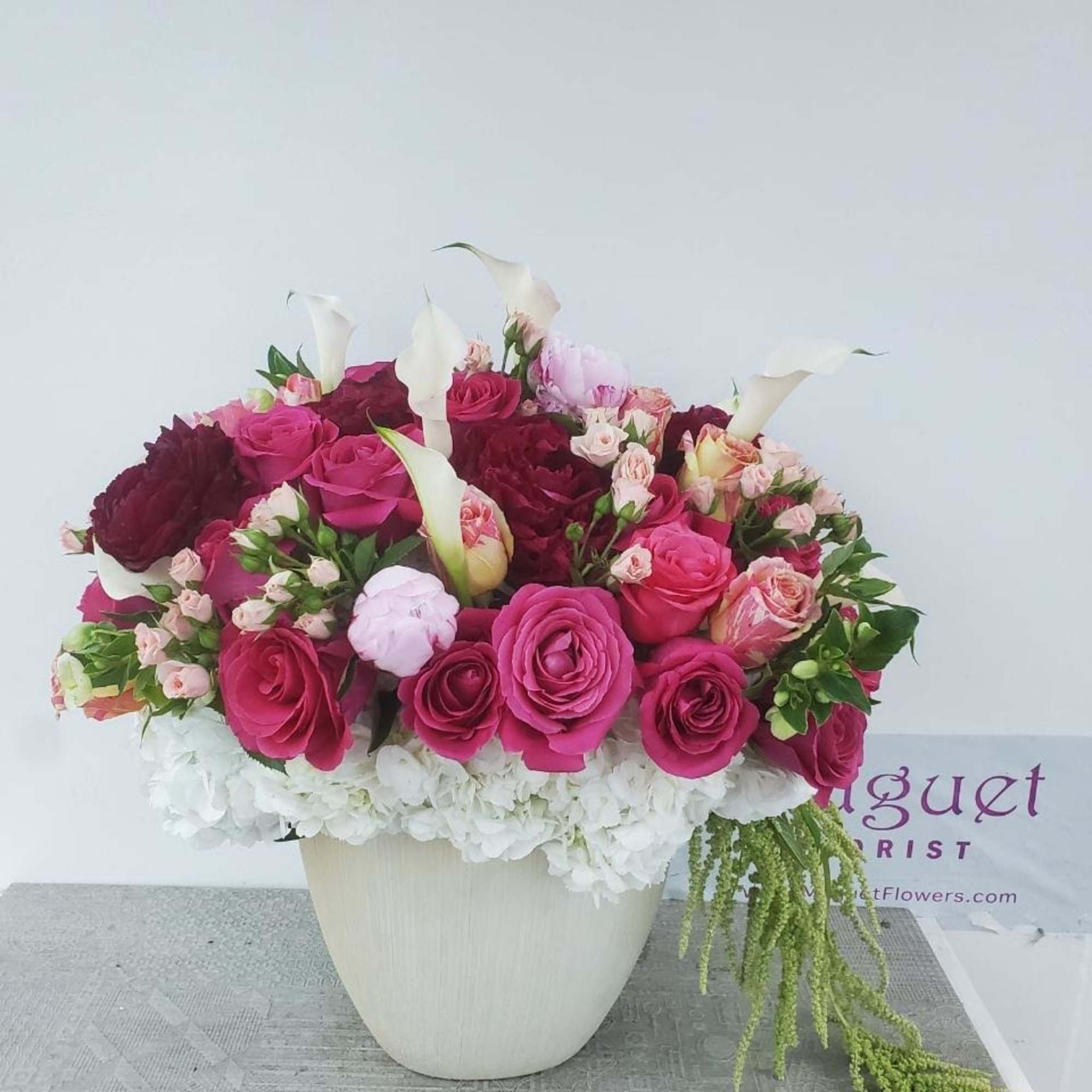 Pink and burgundy rose arrangement with white calla lilies in a white vase