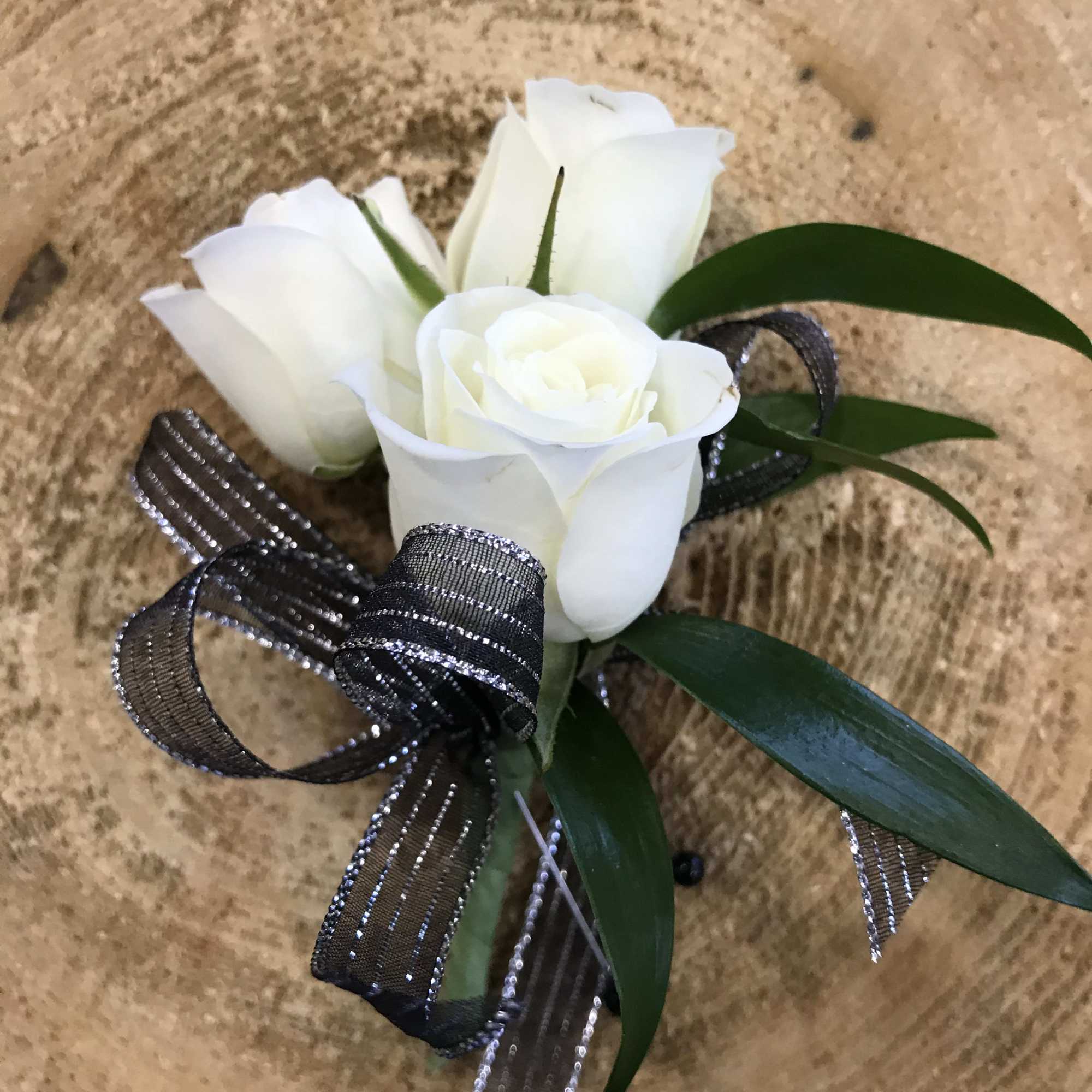 White rose boutonniere with black ribbon on a tan textured background
