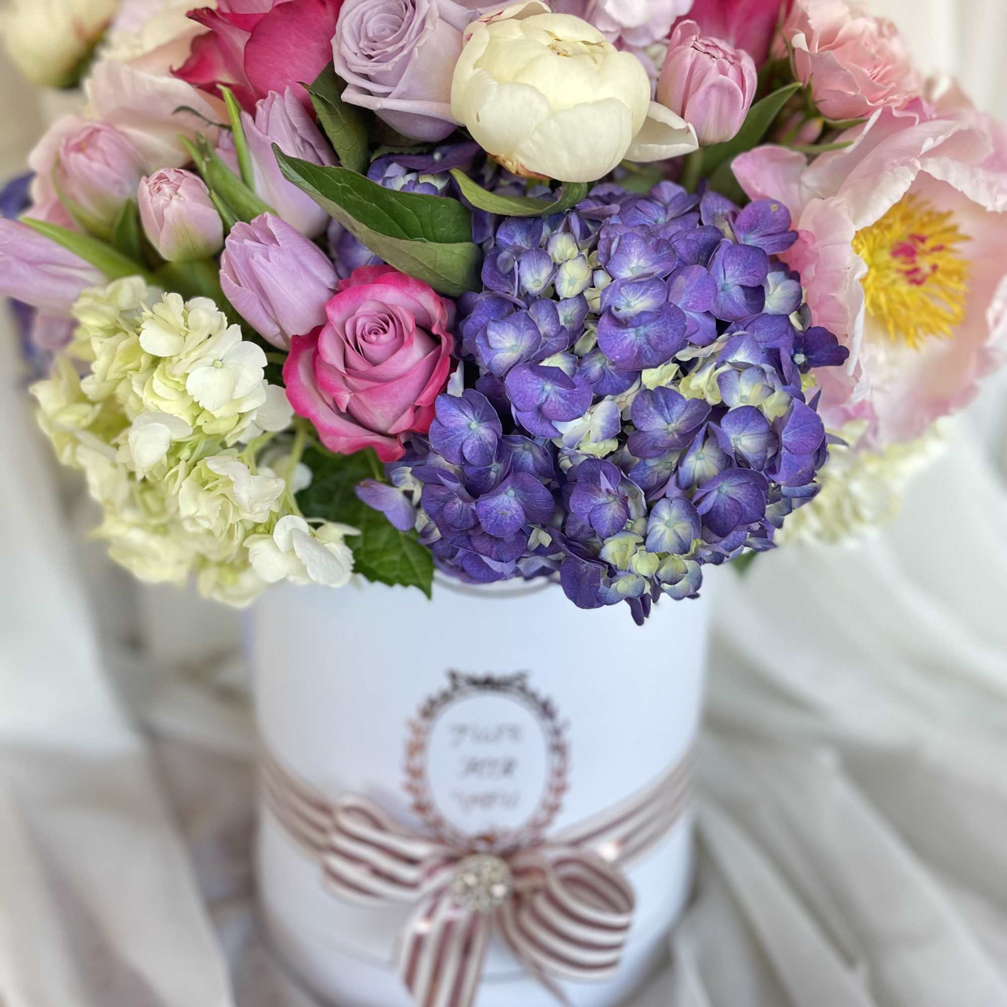 Mixed pink and purple bouquet in a white hatbox with ribbon
