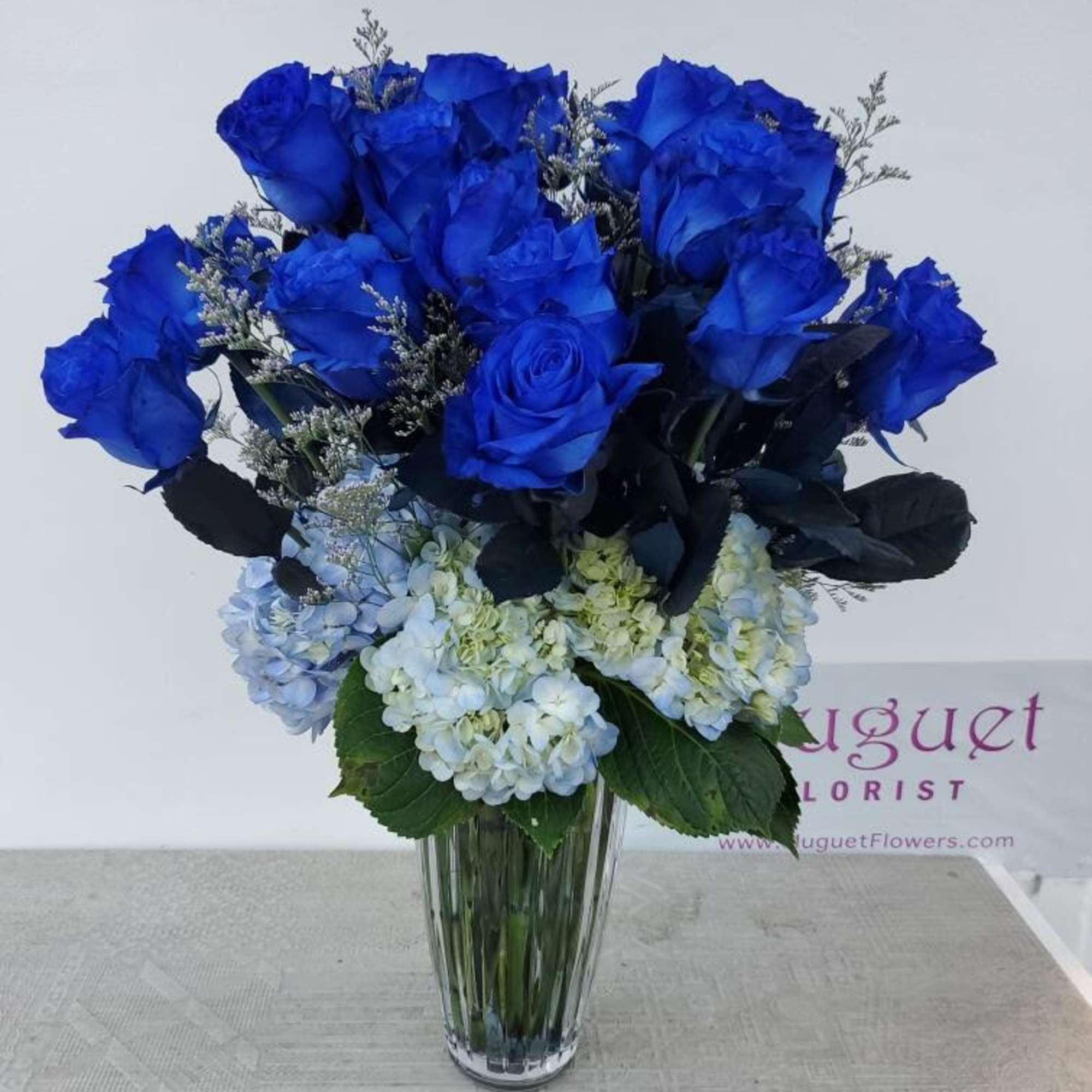 Blue roses and pale hydrangeas arranged in a clear glass vase, photo 3 of 3