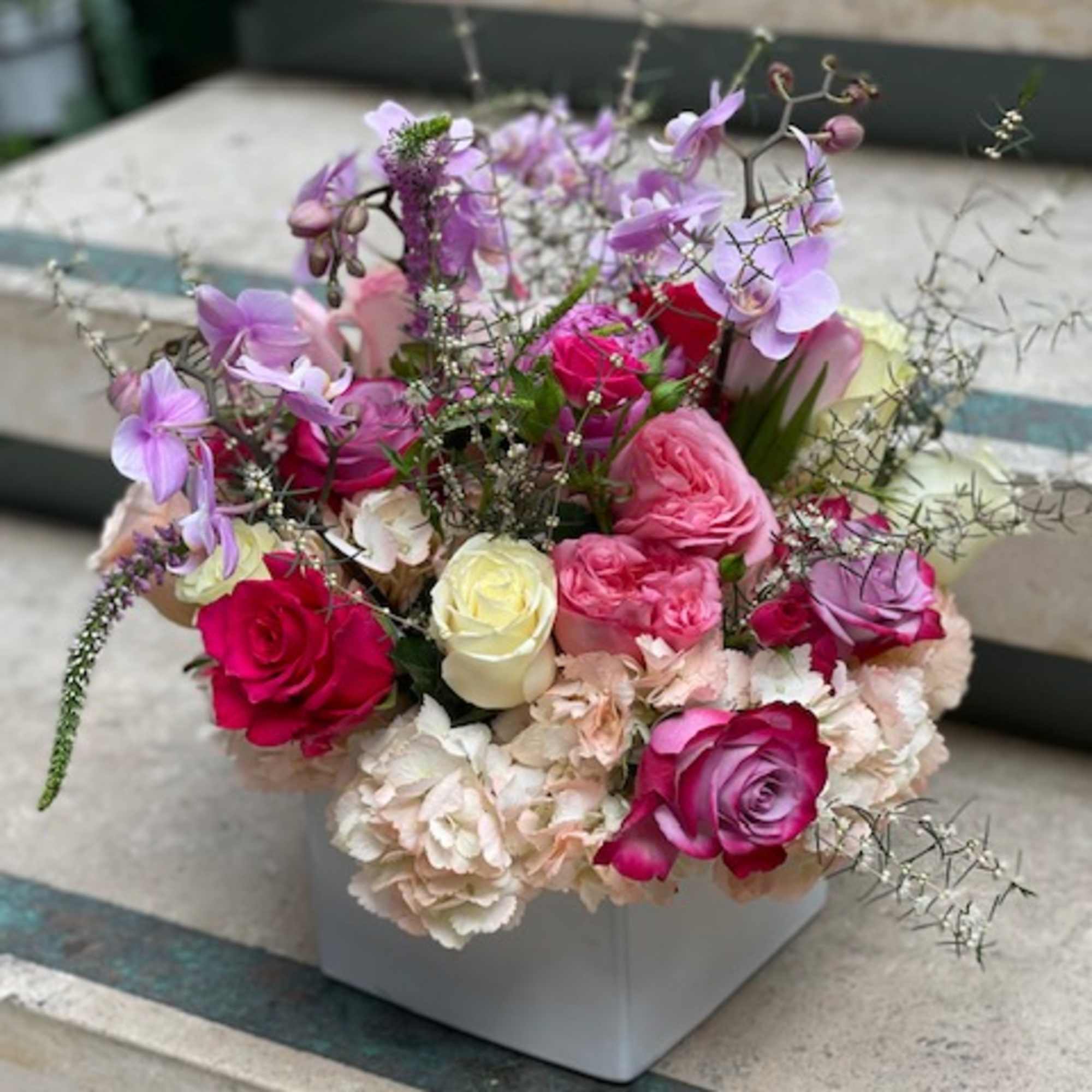 Mixed pink and purple roses in a white square vase