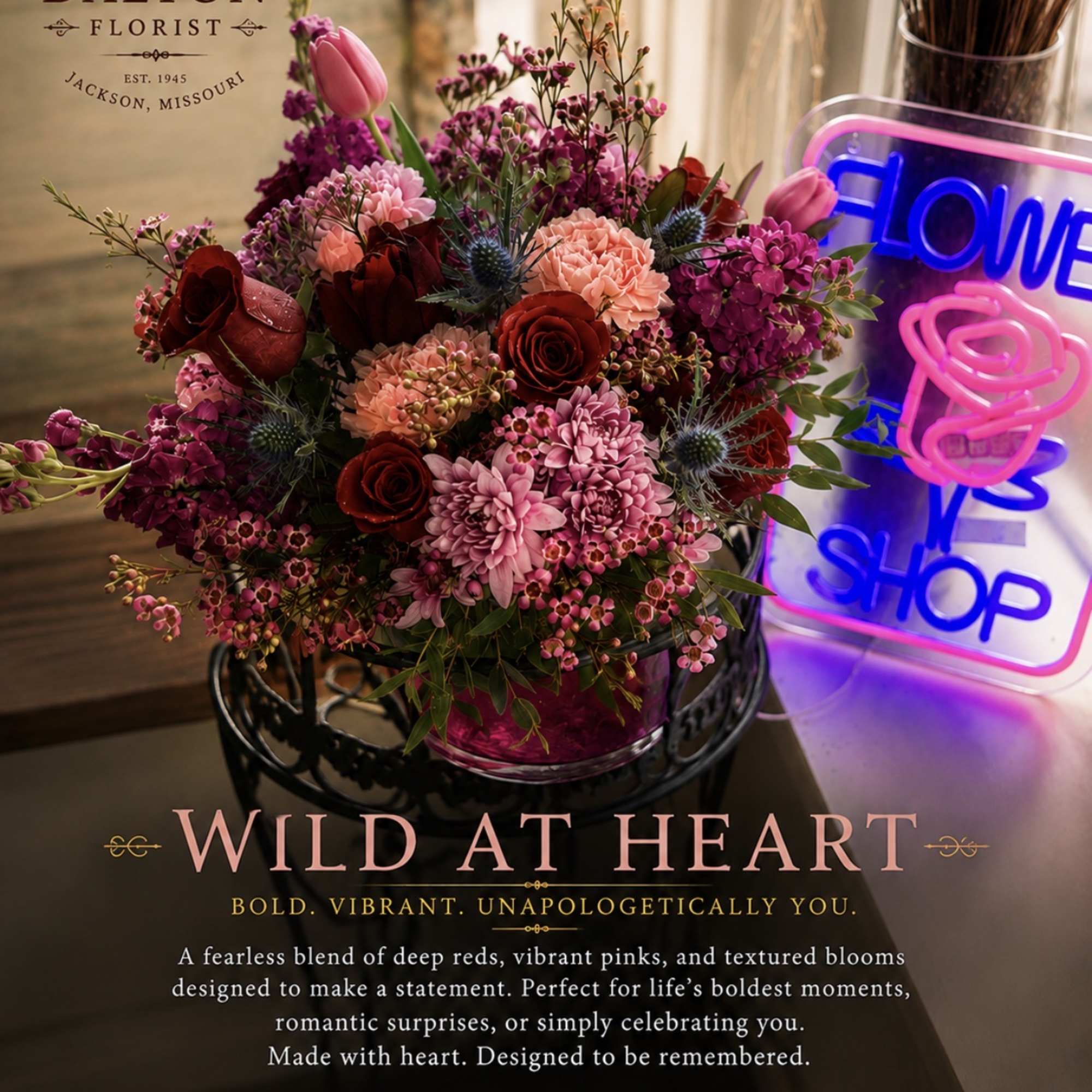 Mixed bouquet of pink and red flowers in a vase beside a neon flower shop sign