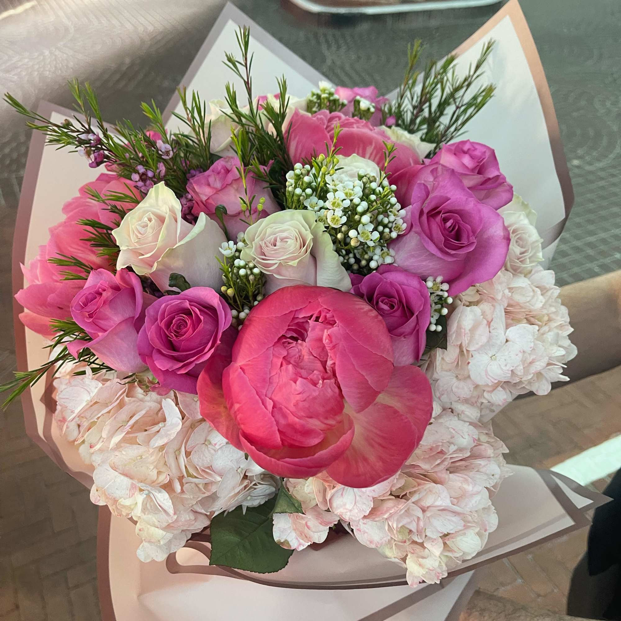 Pink and white bouquet of roses, peonies, and hydrangeas wrapped in paper