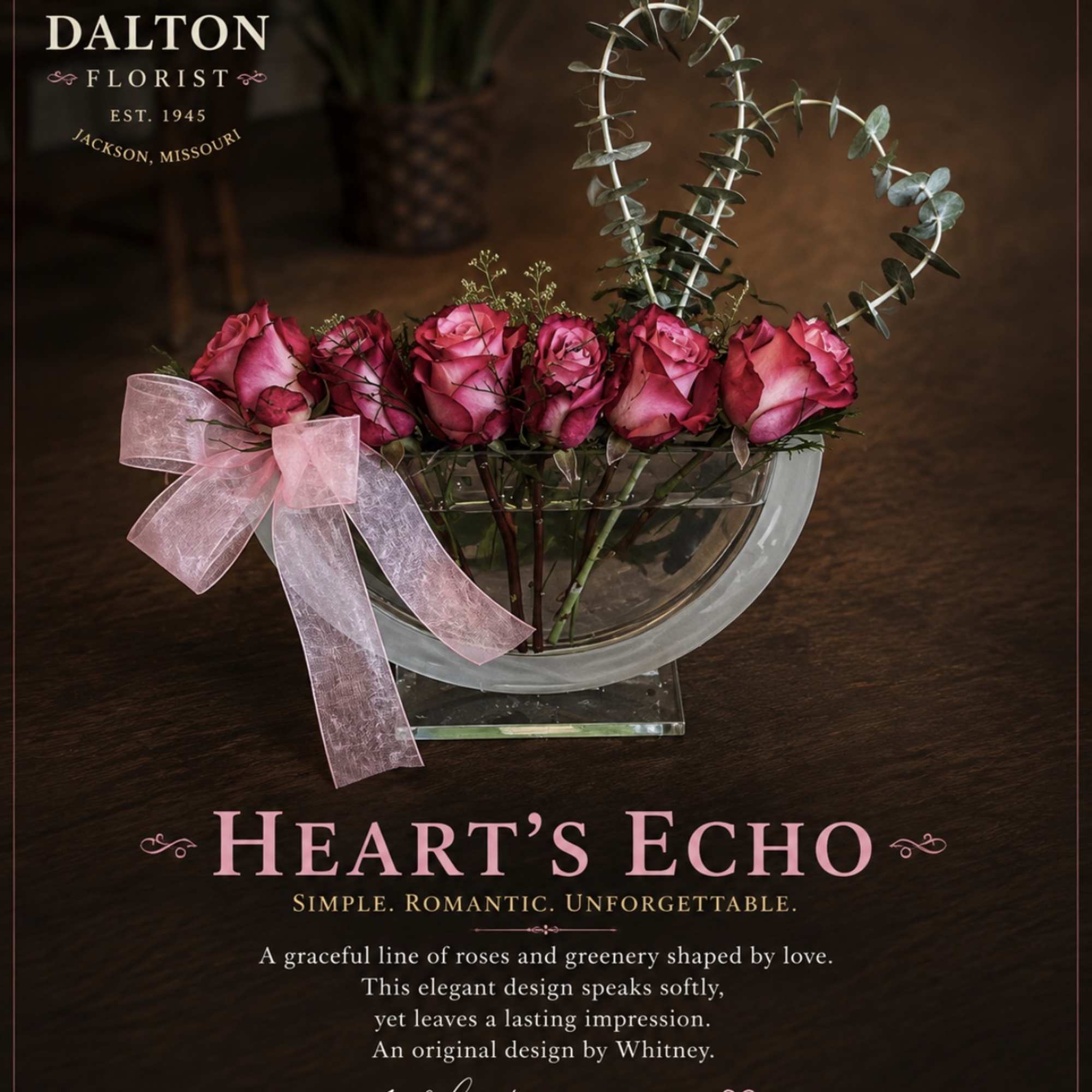 Pink roses in a glass bowl with a pink ribbon and heart-shaped eucalyptus stems