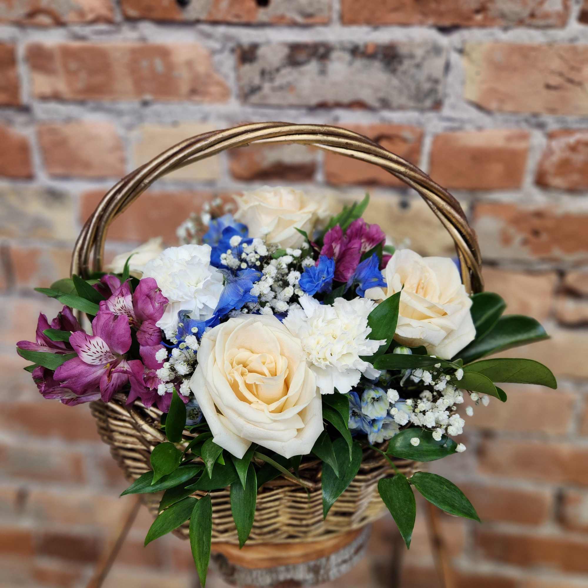 Basket arrangement with cream roses, purple blooms, and blue flowers