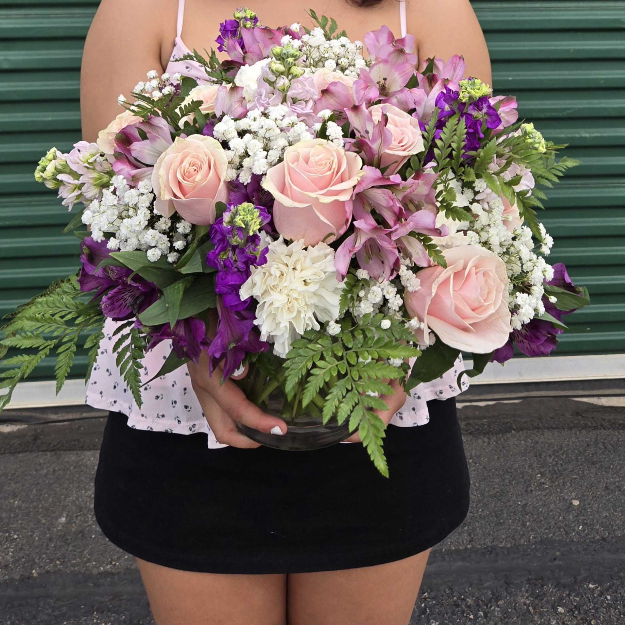 Large bouquet of pink roses, purple flowers, and white filler in a glass vase
