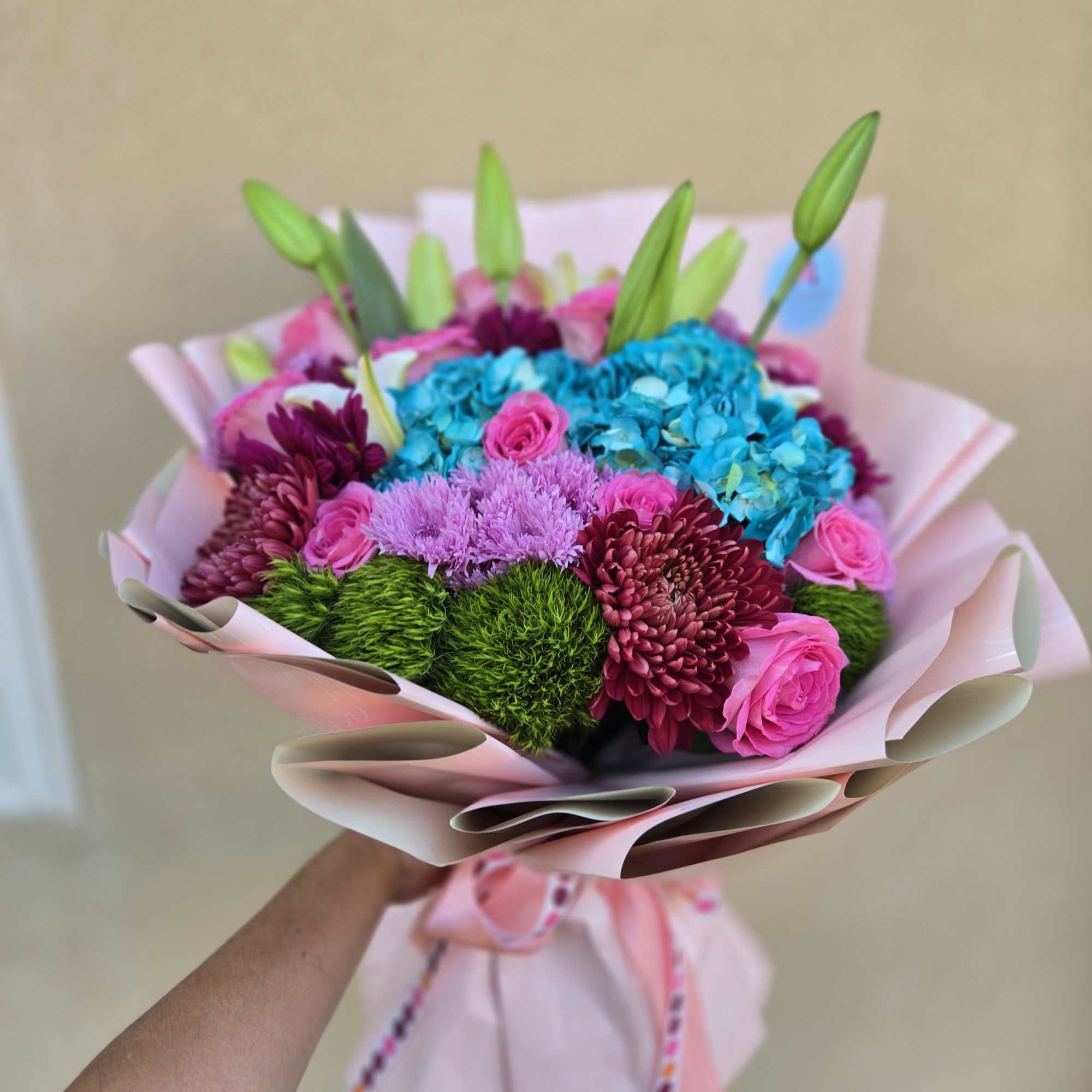 Bouquet of pink roses, blue hydrangeas, and purple chrysanthemums wrapped in pink paper
