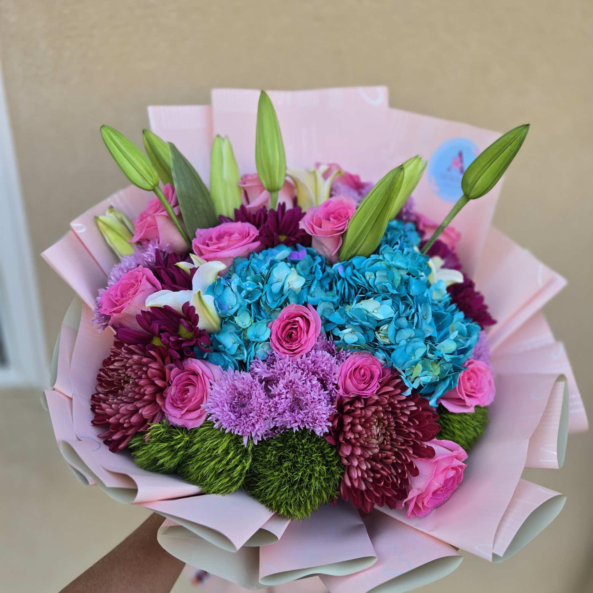 Bouquet of pink roses, blue hydrangeas, and purple flowers wrapped in pink paper