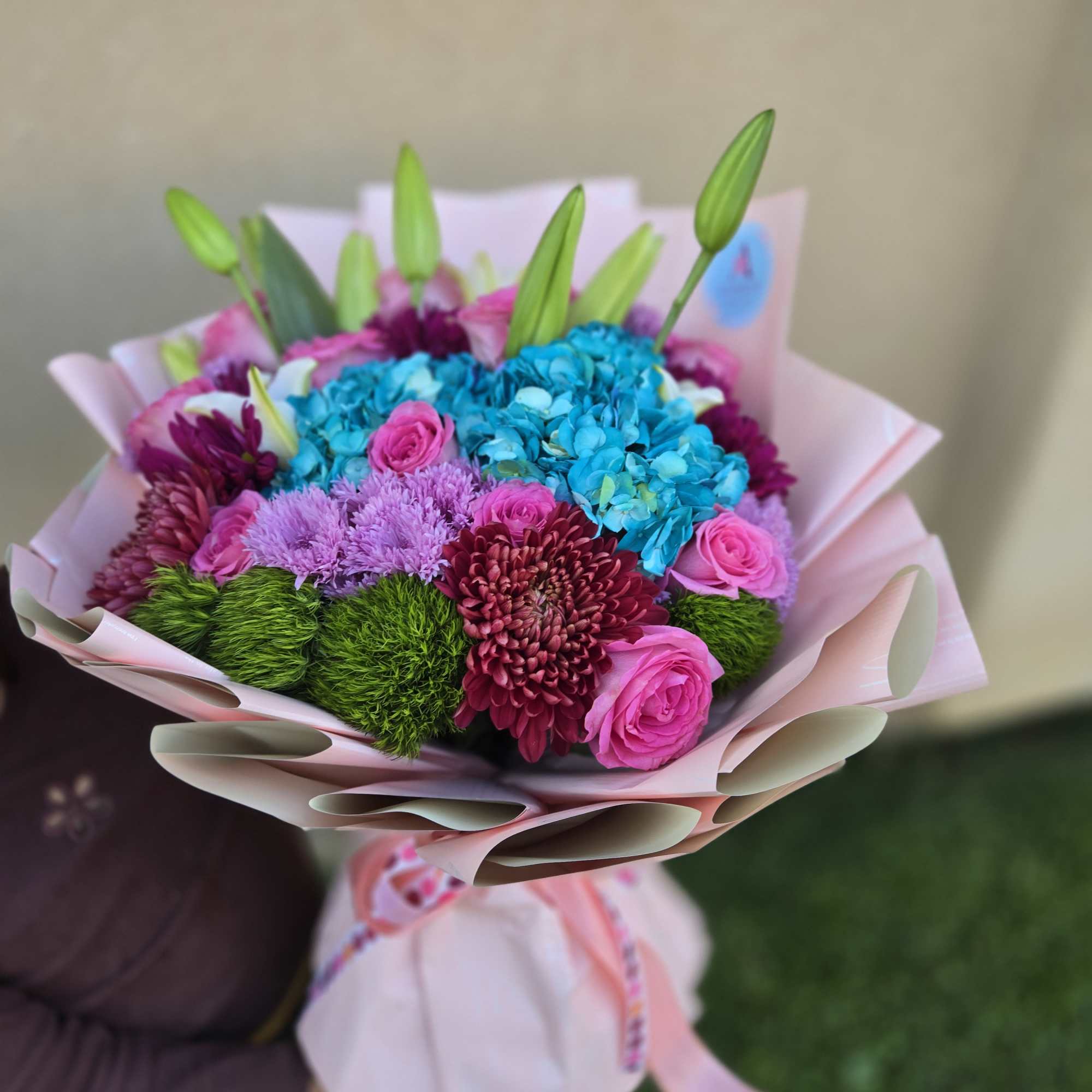 Colorful bouquet of pink roses, blue hydrangeas, and purple blooms wrapped in pink paper
