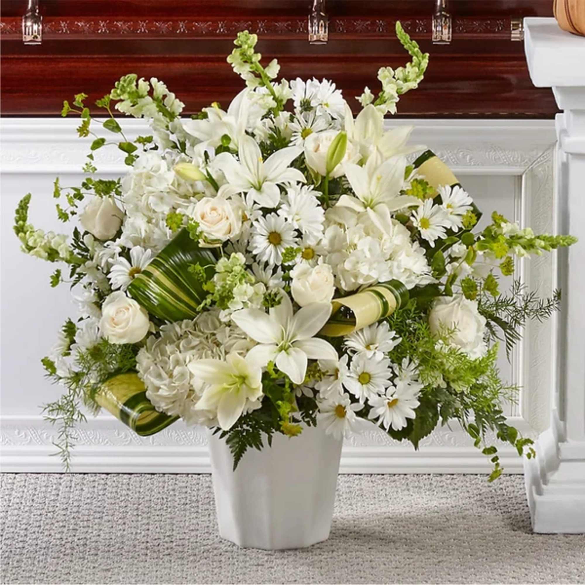 White floral arrangement in a white vase with lilies, roses, and daisies