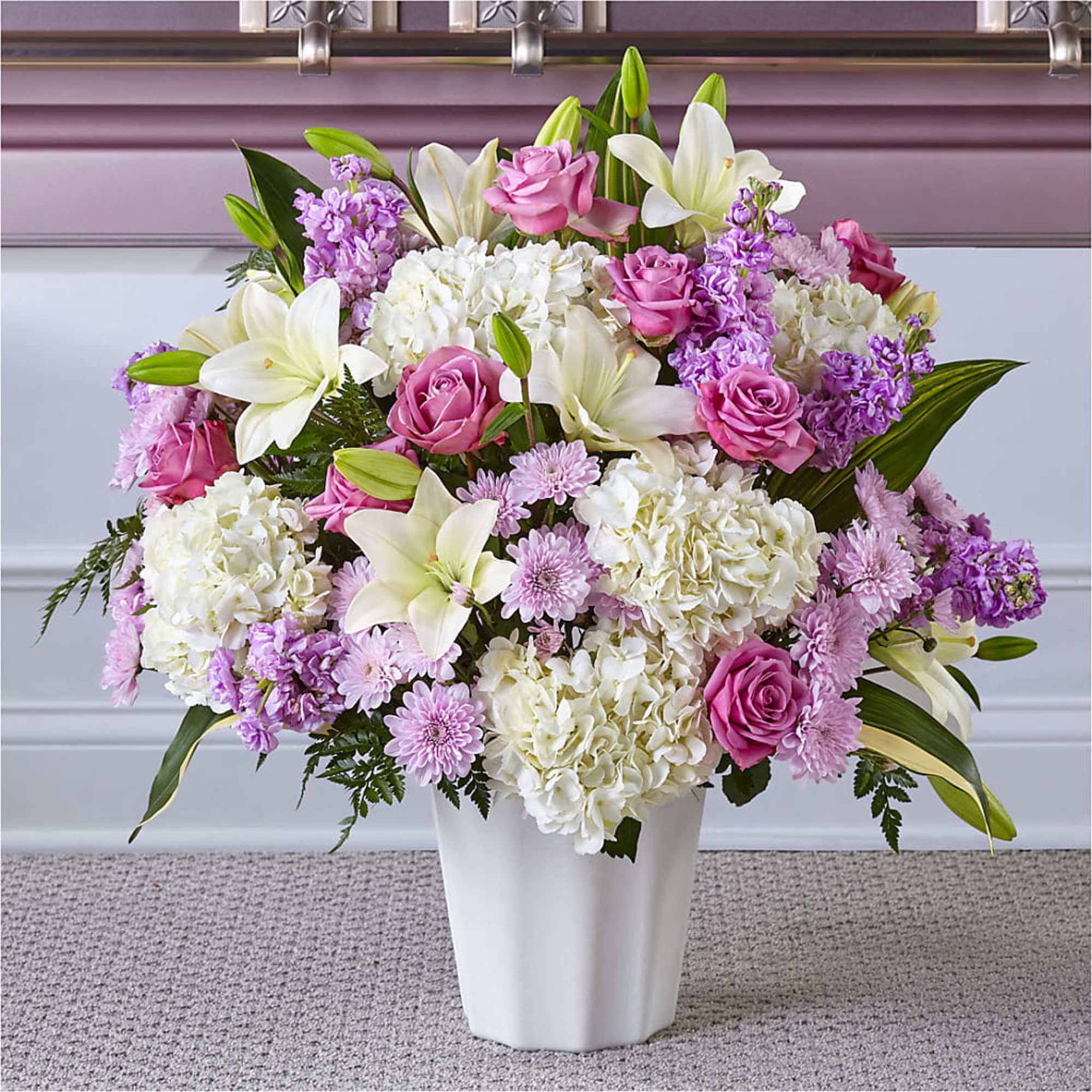 Pink roses and white lilies arranged with white hydrangeas in a white vase