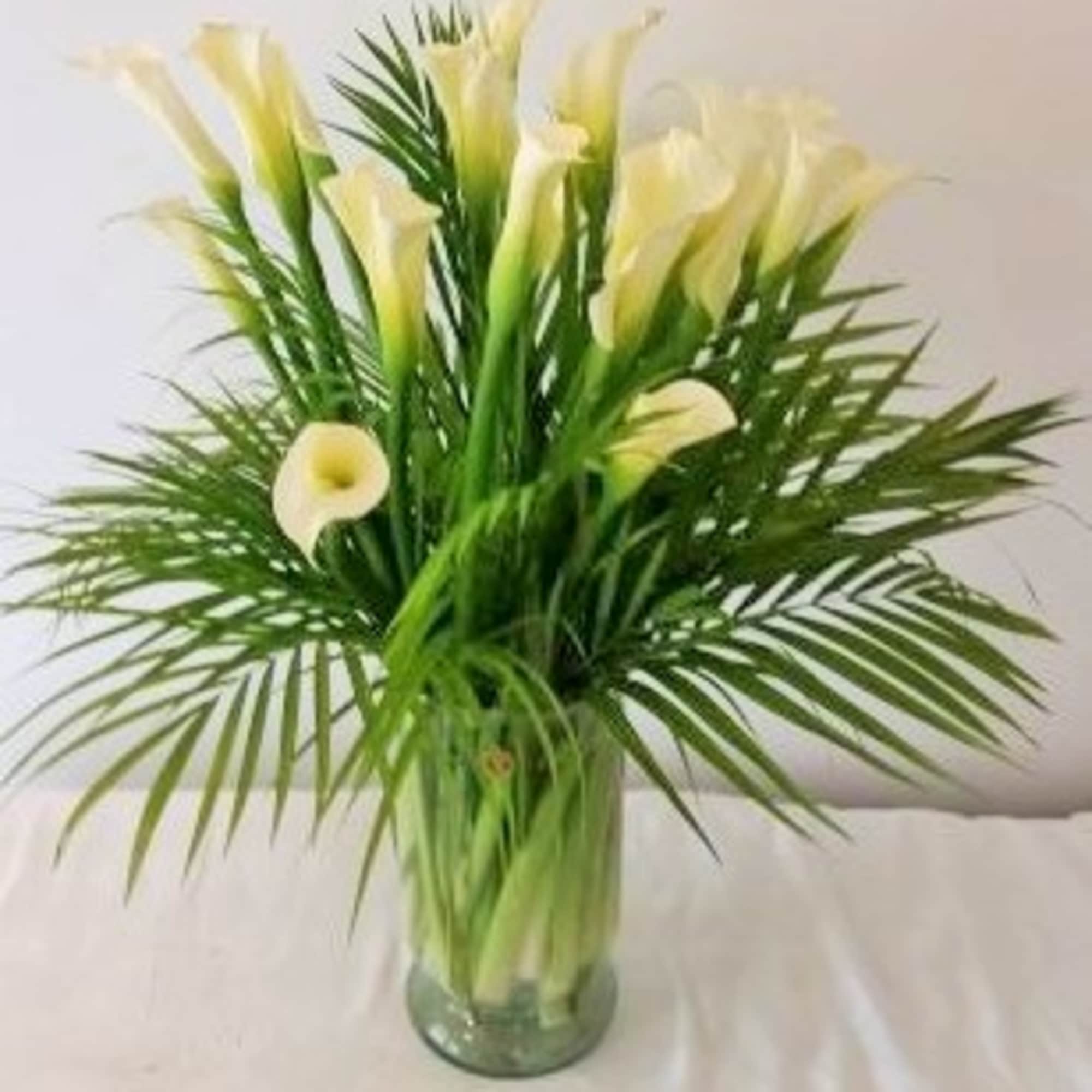 White calla lilies in a glass vase with palm fronds