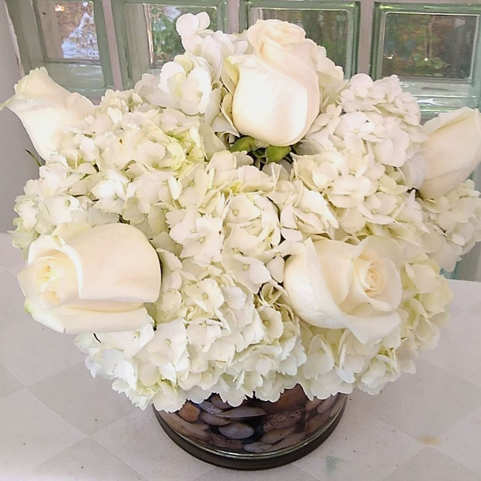 White roses and hydrangeas arranged in a round glass vase