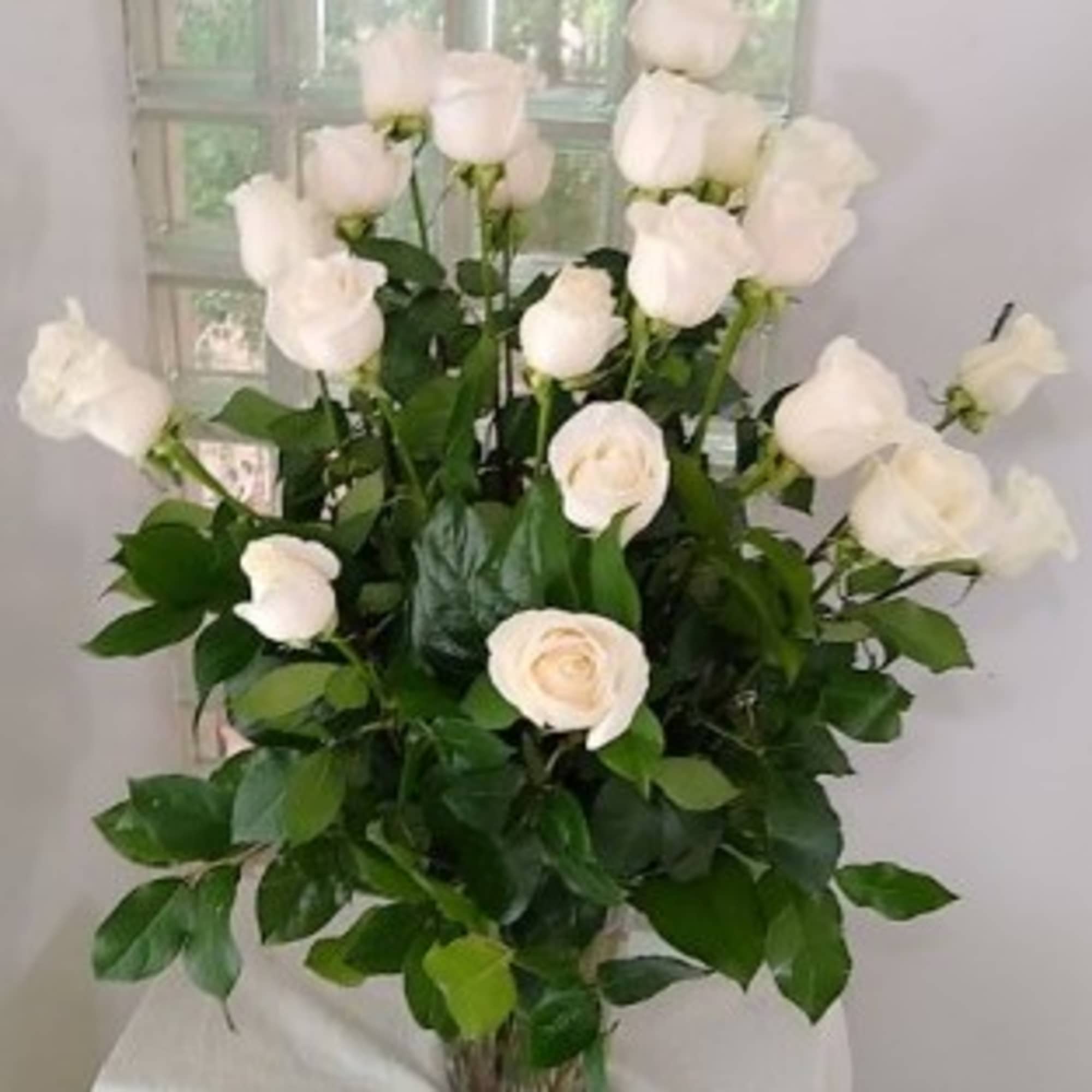 White roses arranged in a glass vase with dense green foliage